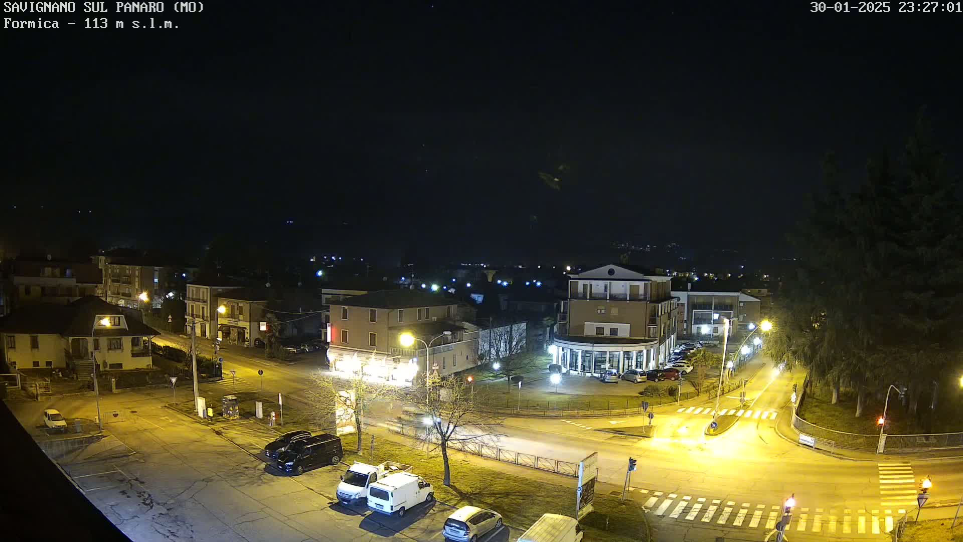 A nighttime aerial view of a town square with several buildings and cars, under a clear, dark sky.