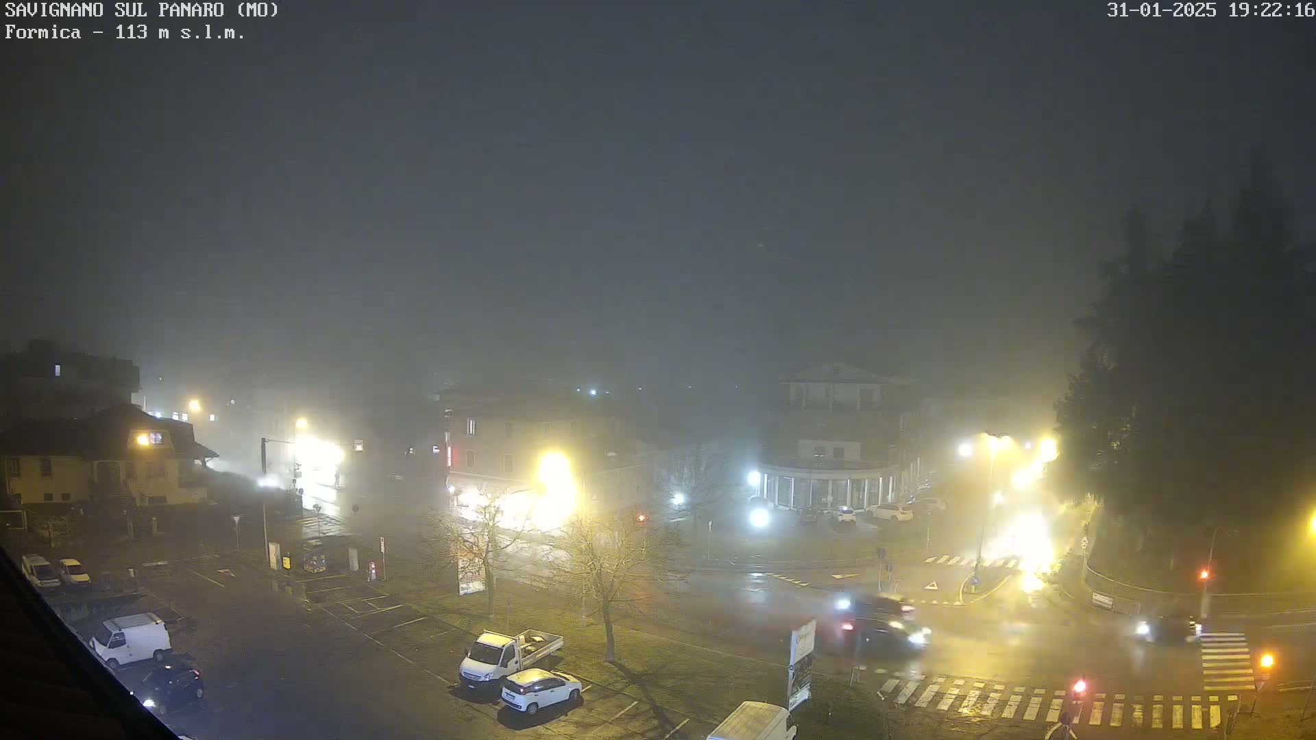 A foggy night scene shows a town square with cars and buildings illuminated by streetlights.