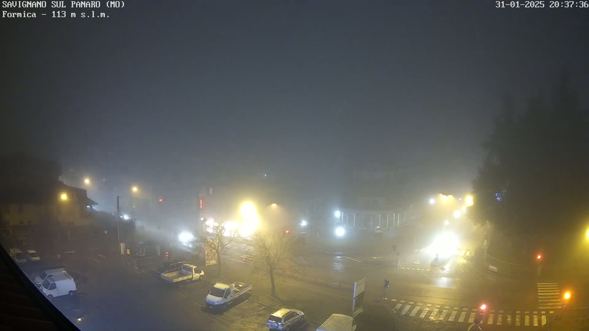 A foggy night scene shows a street intersection with cars and streetlights, viewed from above.