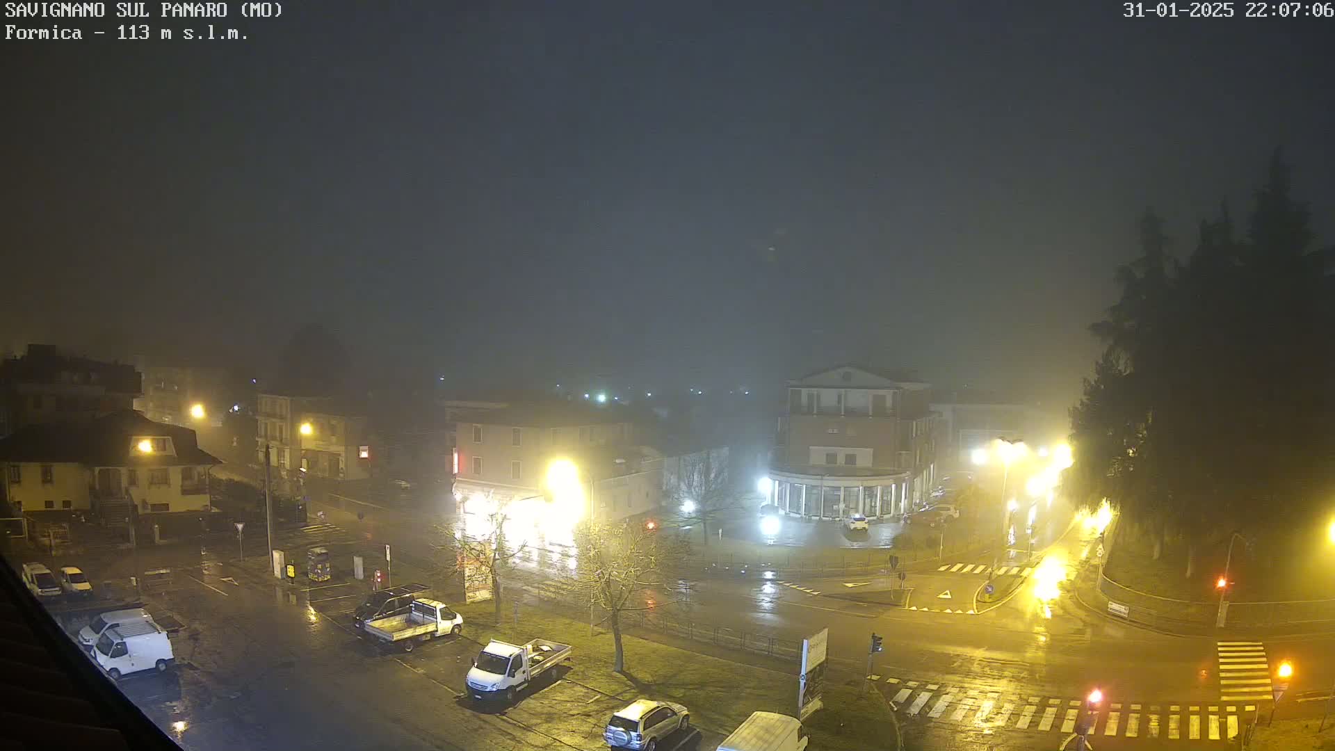 A nighttime, foggy, rain-slicked town square scene shows several buildings, parked cars, and streetlights illuminating the wet streets.