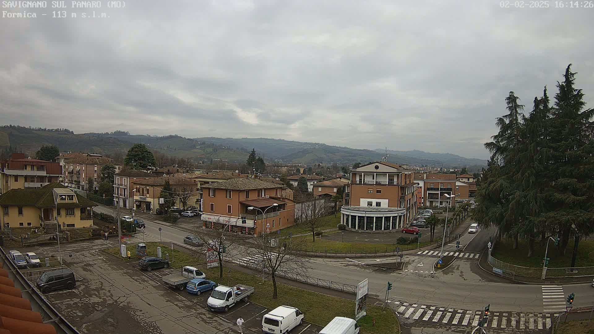 An overcast day reveals a view of a town nestled in a valley, with cars parked in a lot and several buildings visible, including some two-story structures.