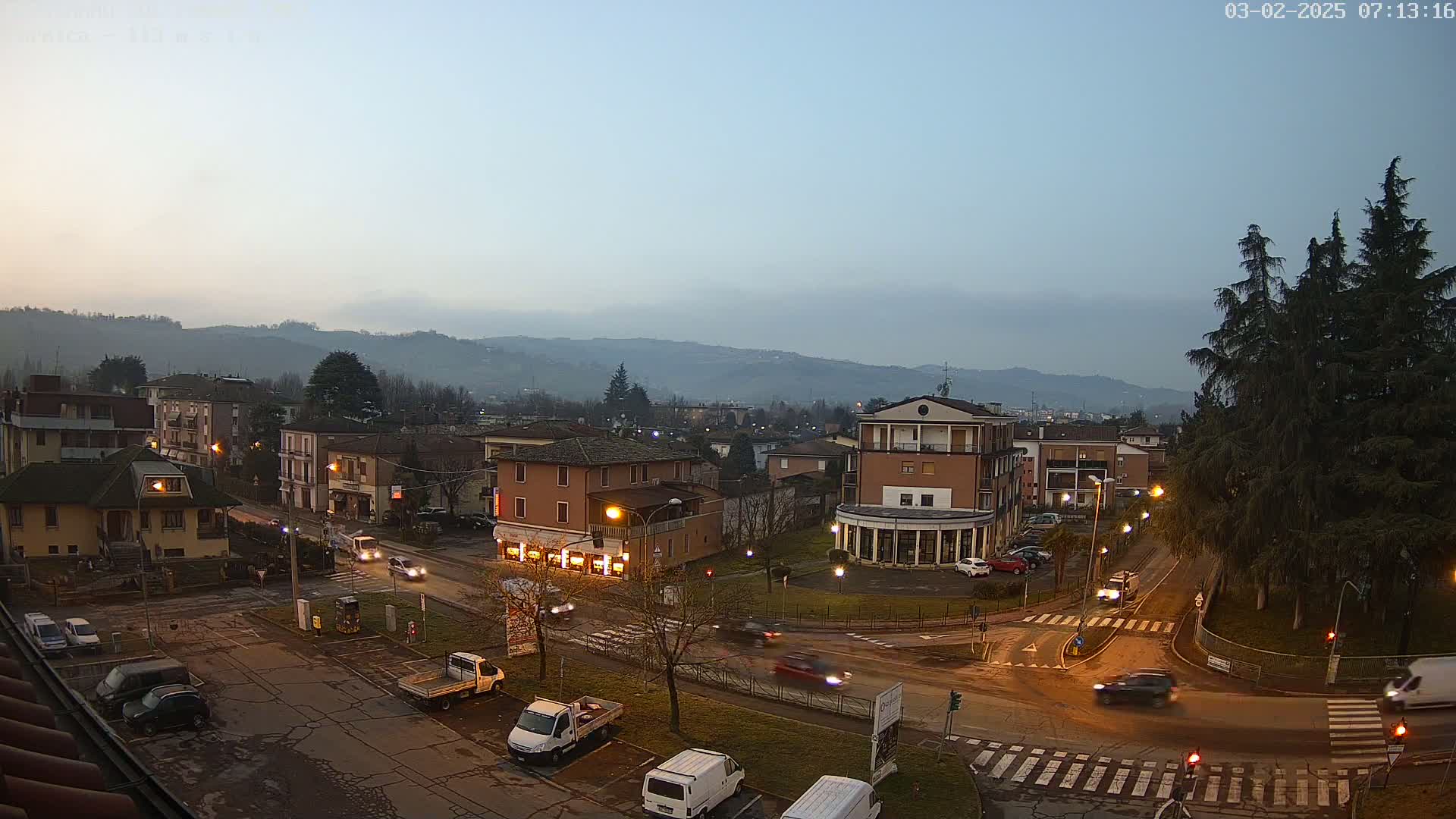 A twilight view of a town square with several buildings and cars, set against a hazy mountain backdrop.