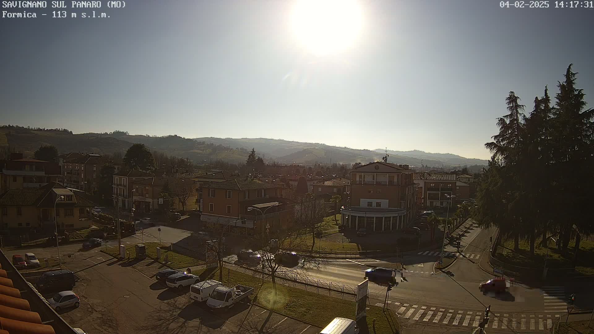 A sunny day reveals a town nestled in a valley, with buildings lining streets and hills rising in the background.