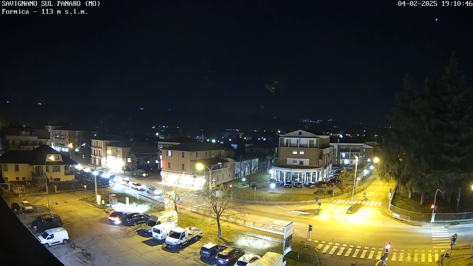 A nighttime aerial view of a town square with cars parked and driving on roads under a clear sky.
