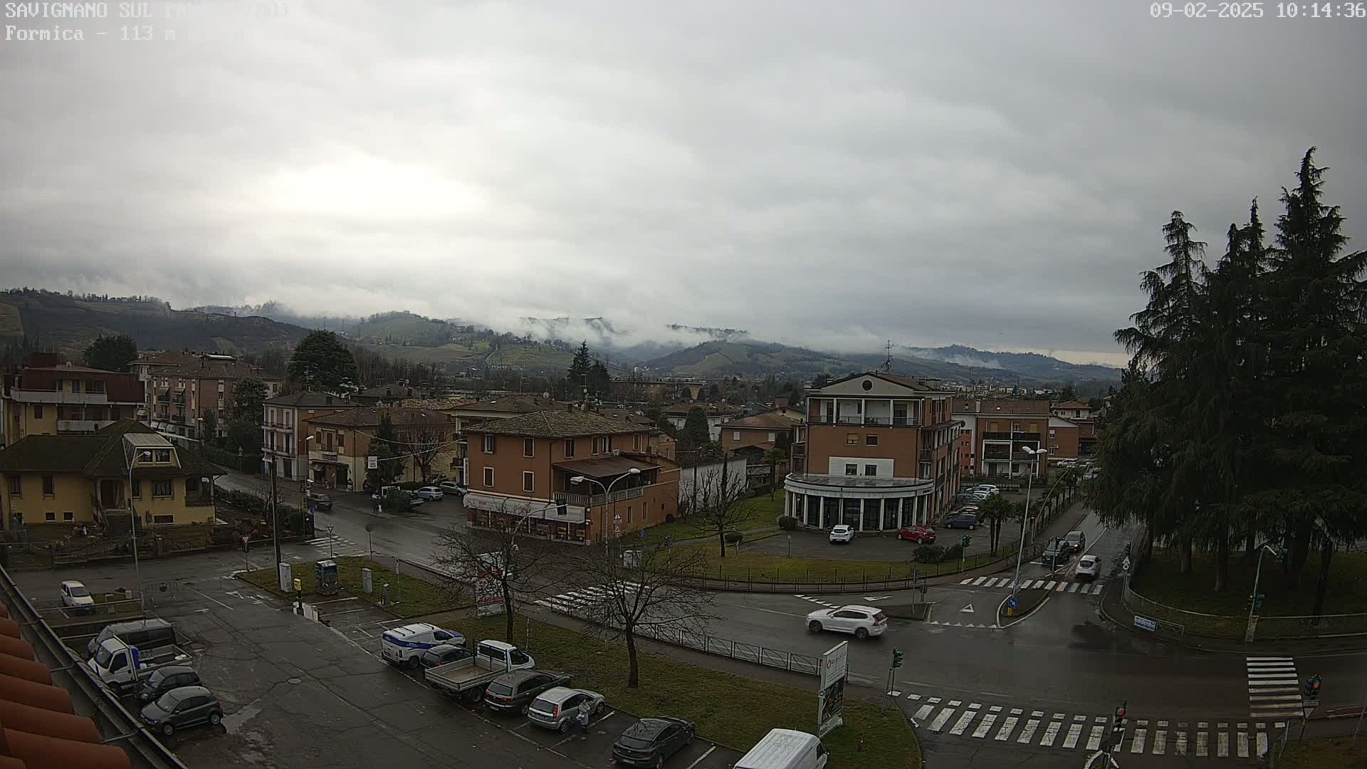 A cloudy day reveals a town nestled amongst low hills, with a wet road and cars parked in a lot.