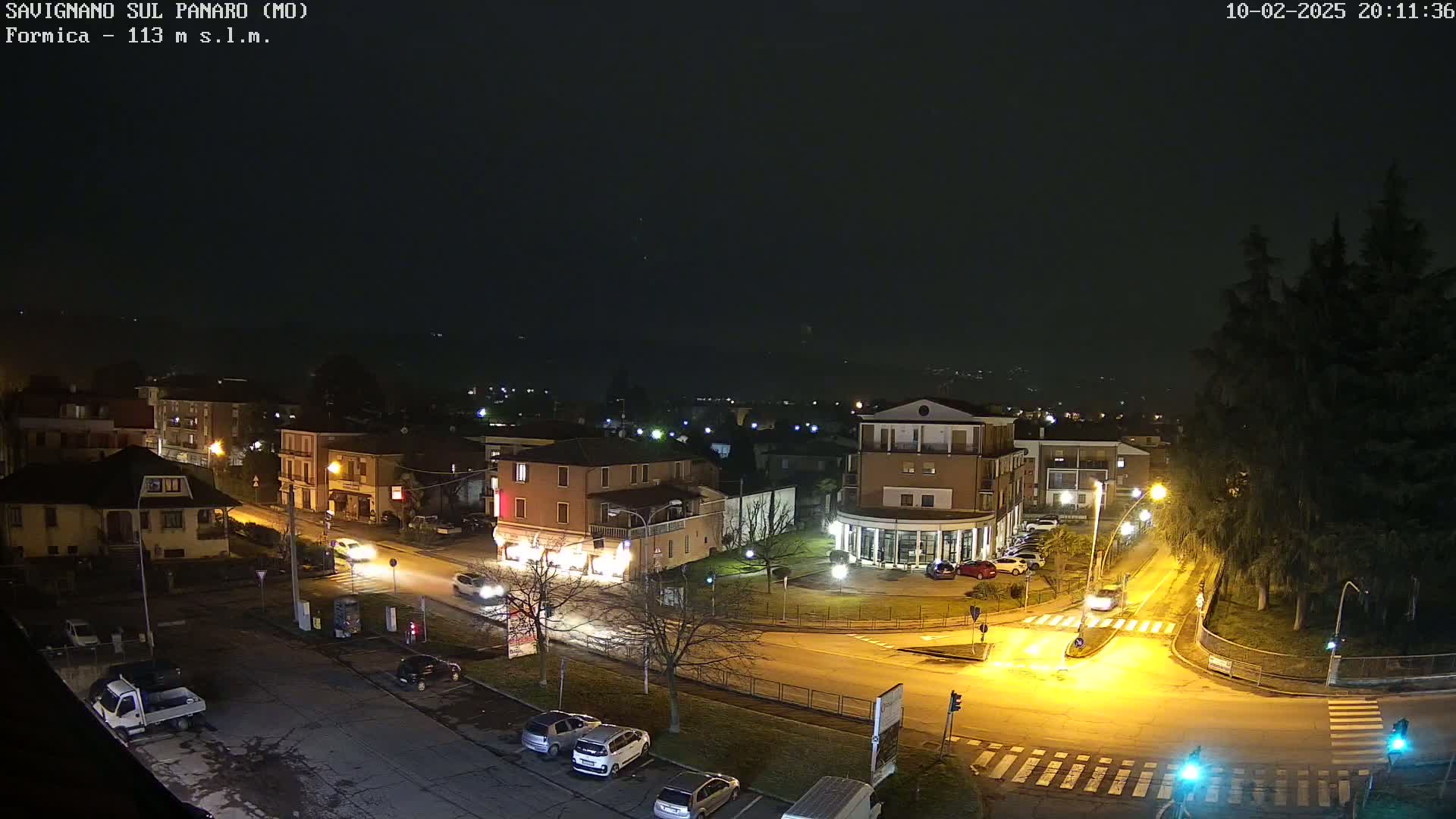 A nighttime, overhead view of a town square with several cars and buildings illuminated under a dark sky.