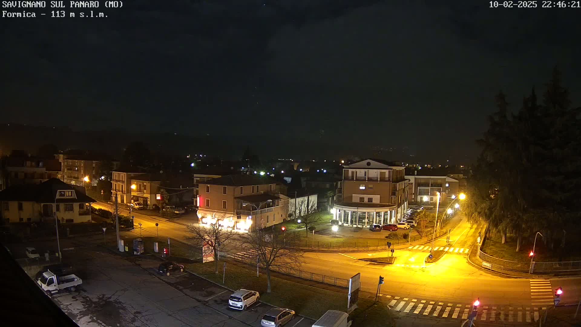 A nighttime, aerial view of a town square with several buildings illuminated, under a dark, cloudy sky.