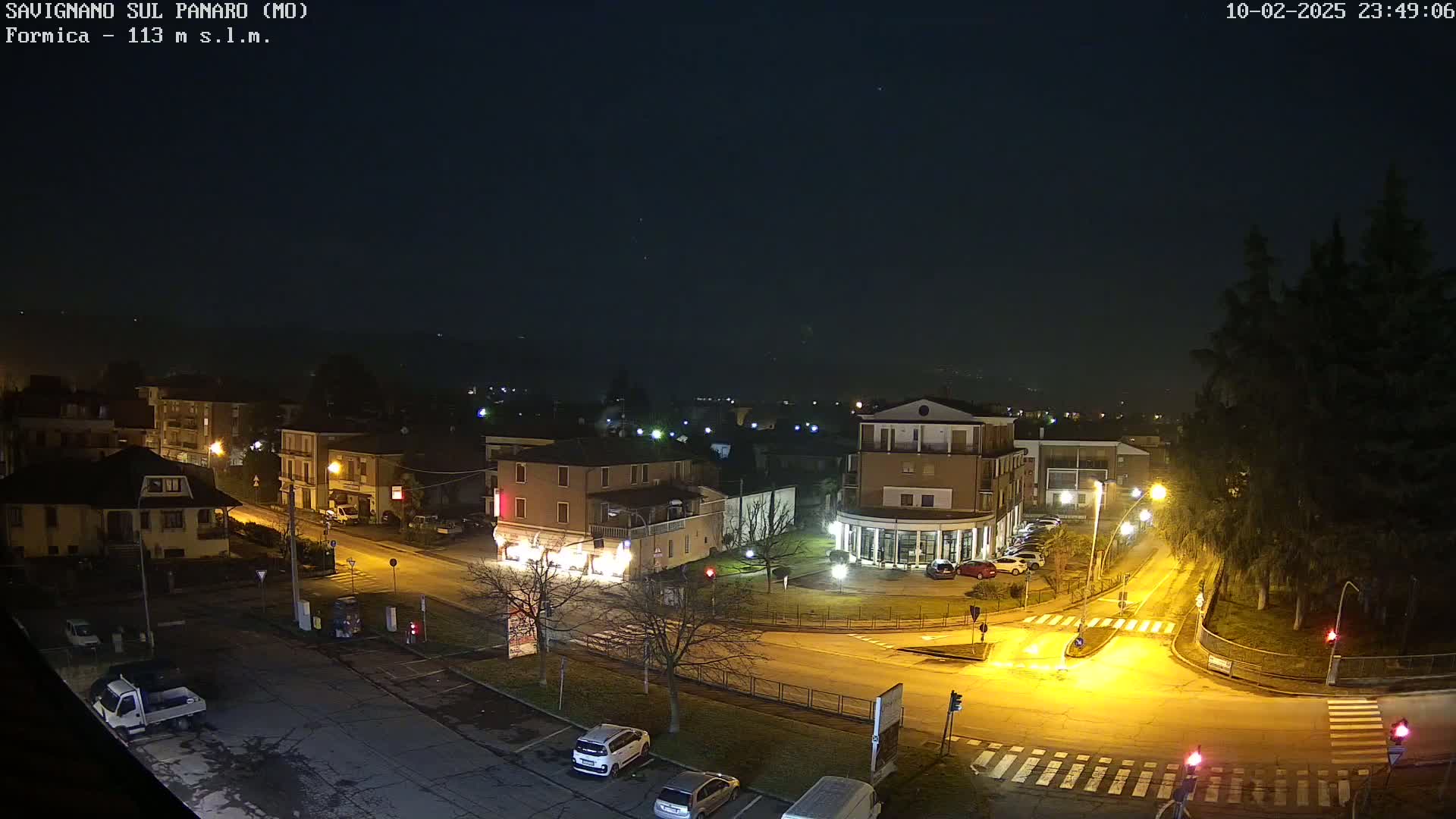 A nighttime, aerial view of a town square with several buildings, cars, and streetlights illuminated under a clear, dark sky.