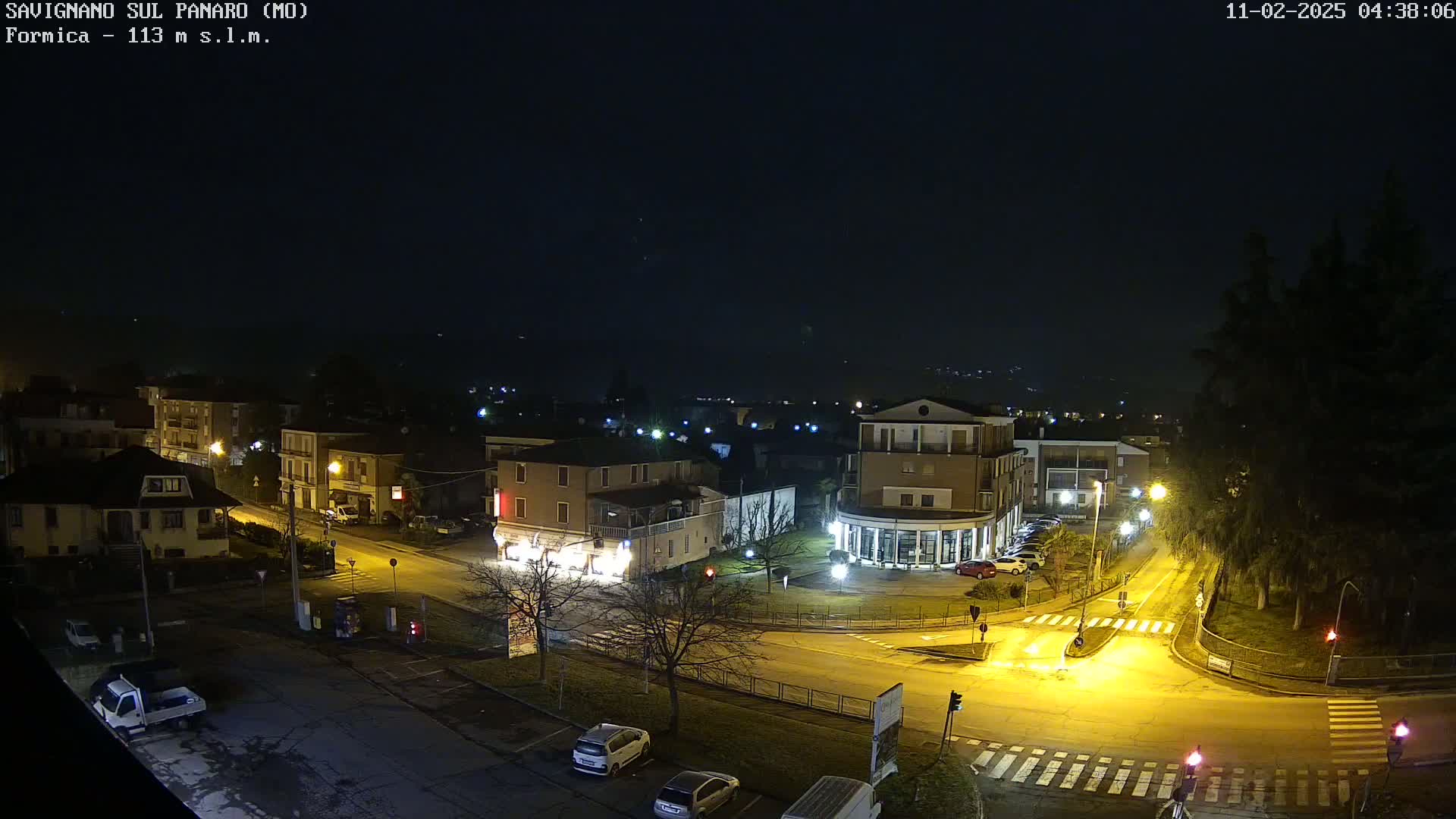 A nighttime, high-angle view of a town's street intersection and surrounding buildings under a dark sky.