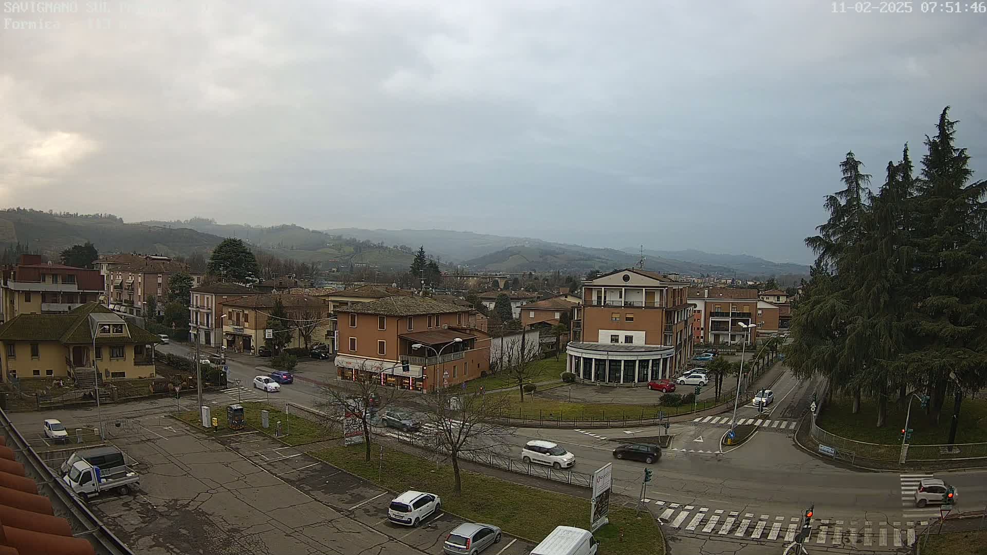 A view of a town nestled in a valley under a cloudy sky, with cars visible on roads and in parking areas.