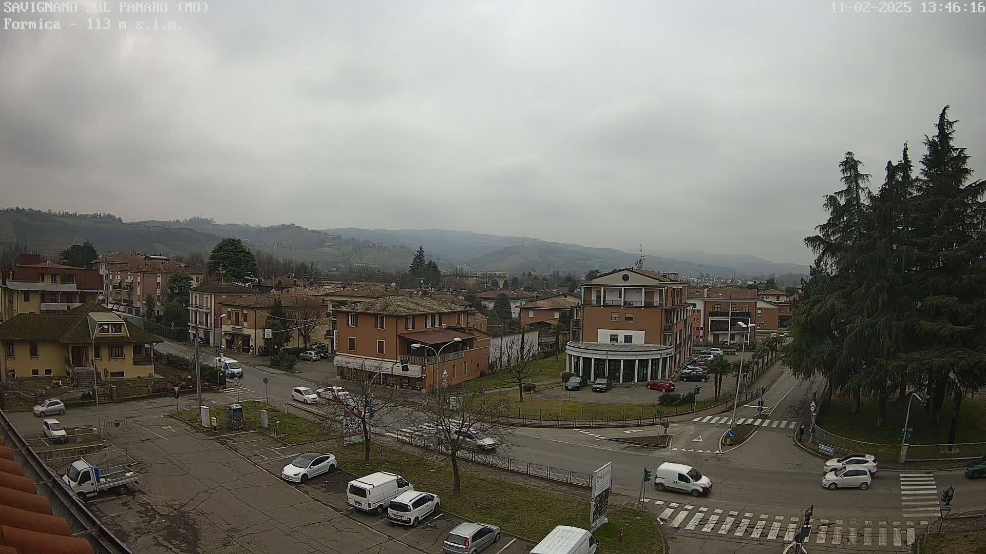 An overcast day reveals a town nestled in a valley, with cars parked in a lot and driving on roads that intersect near a small park.