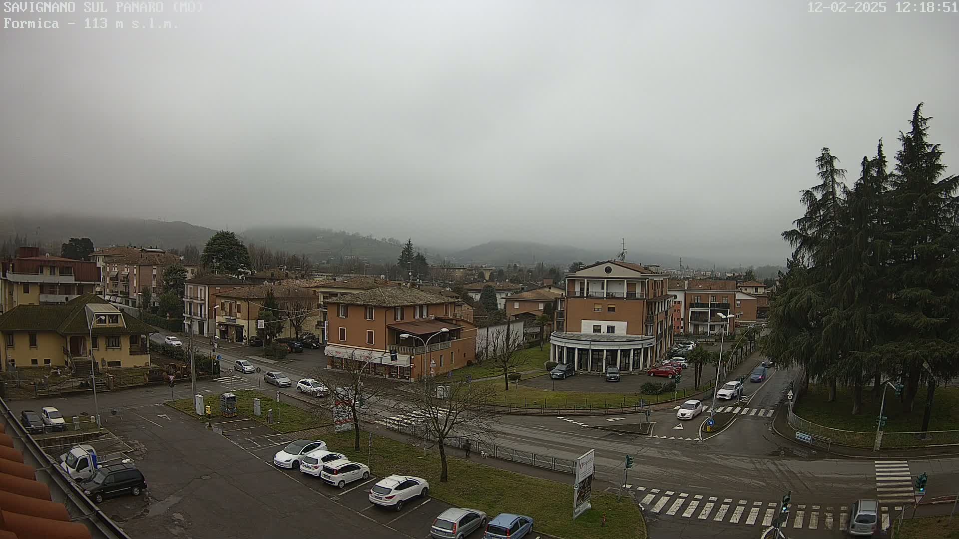 A foggy view of a town, showing several buildings, parked cars, and a roadway intersection.