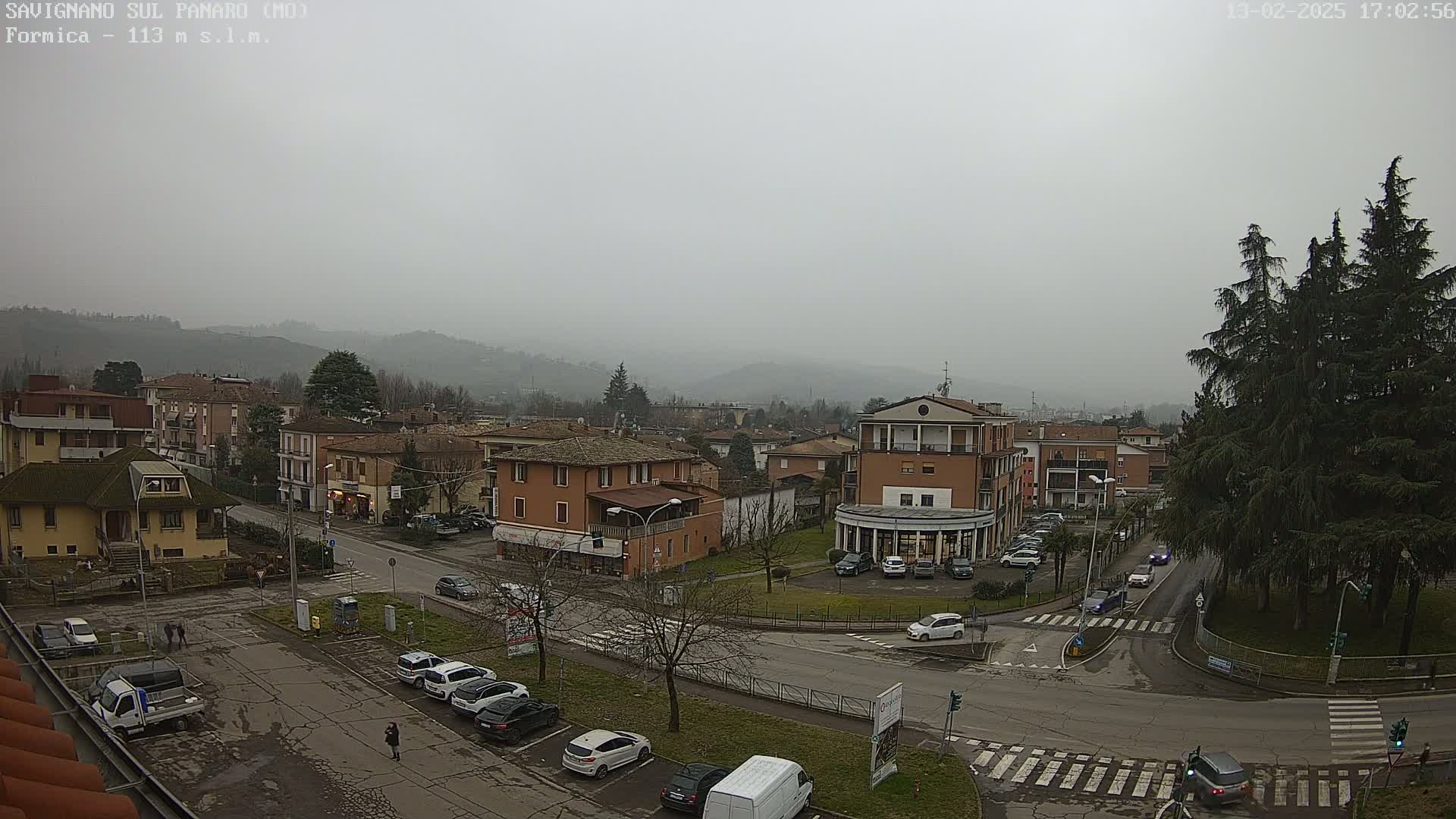A hazy, overcast view of a town square and surrounding buildings, with cars parked in lots and driving on the roads.