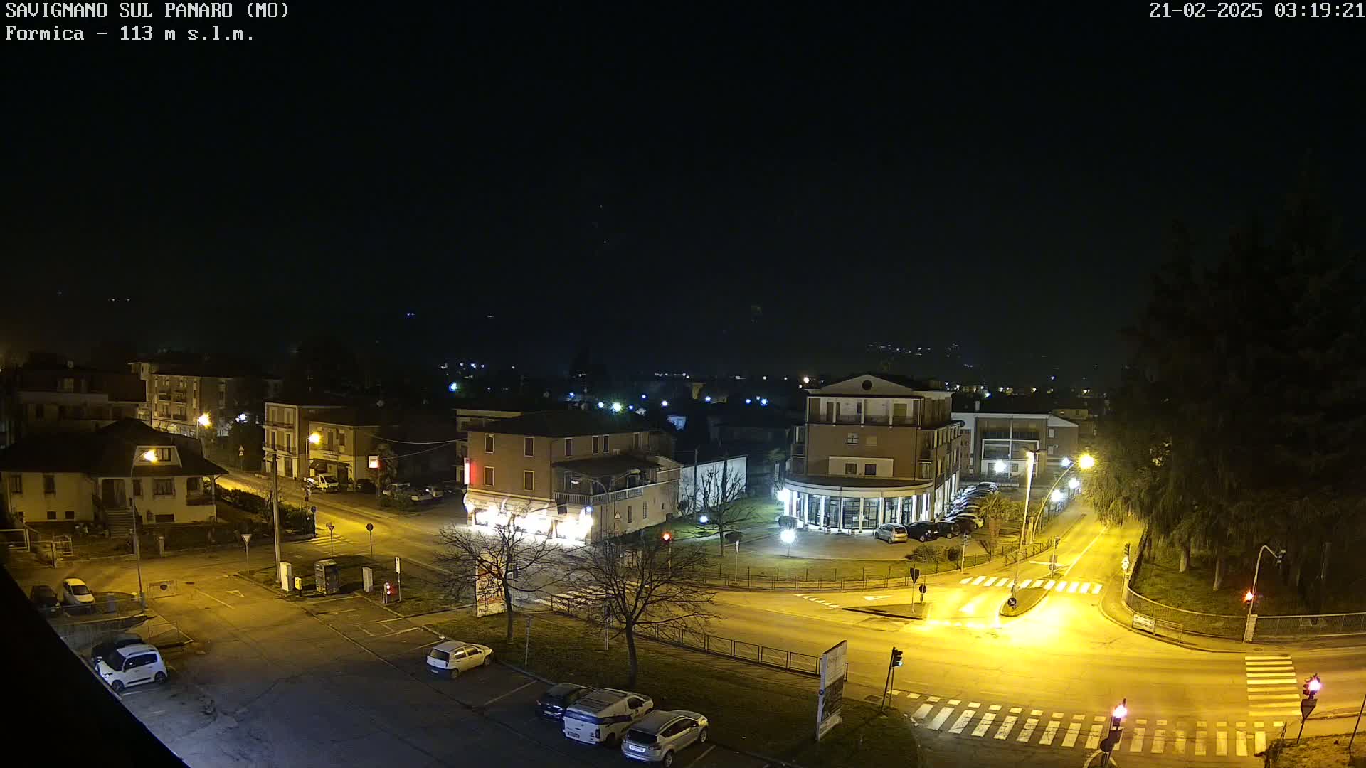 A nighttime aerial view of a town square with cars parked along the streets and buildings illuminated by streetlights.