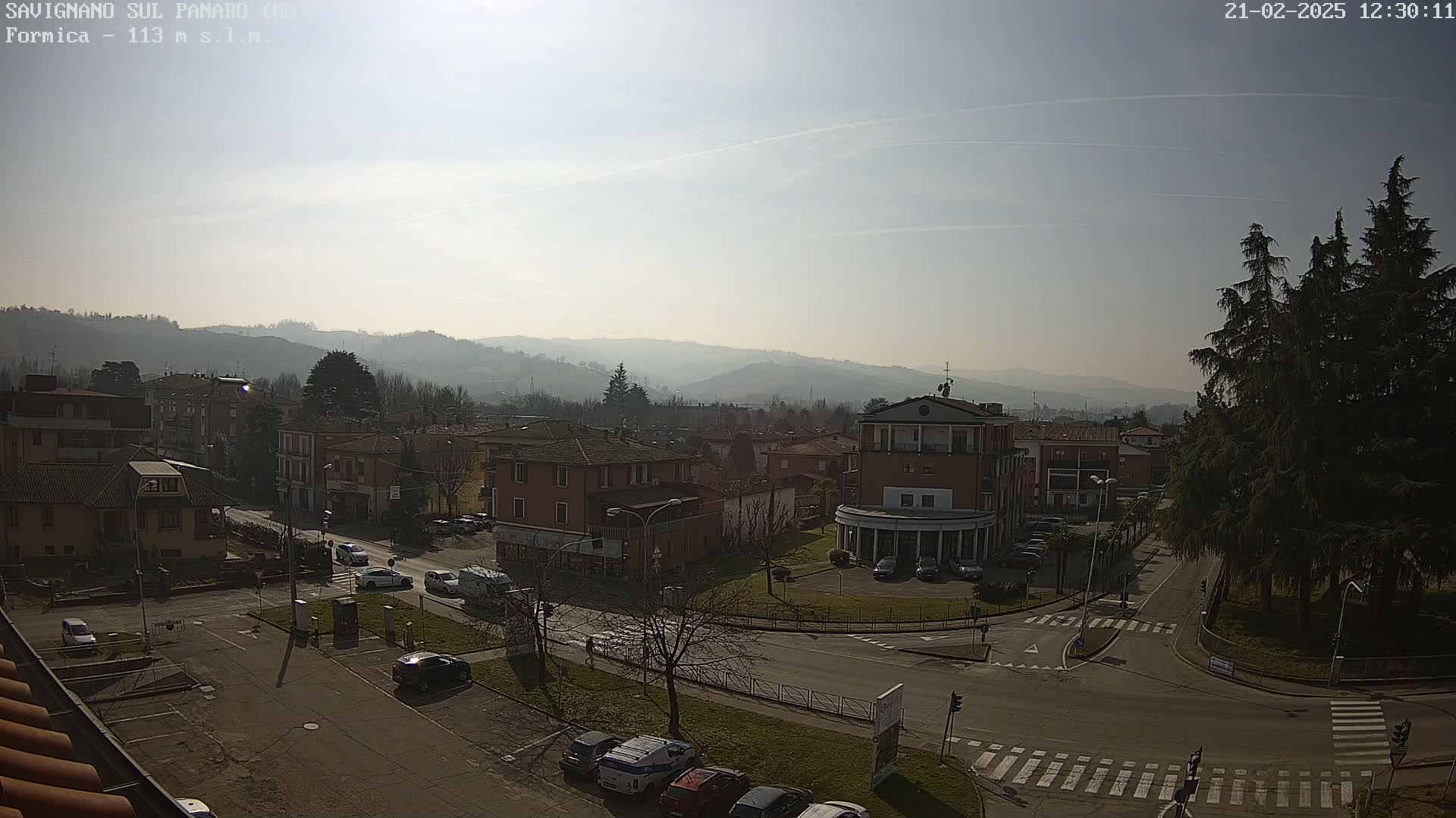 A hazy, sunny day reveals a small town nestled in a valley surrounded by low, distant mountains, with cars parked in a street-level parking lot.