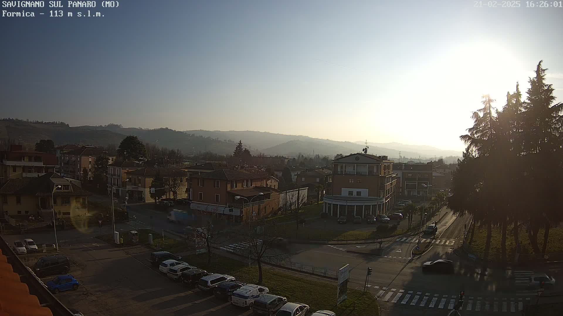 A sunny day reveals a view of a town nestled in a valley, surrounded by hills and featuring several cars parked along the streets.