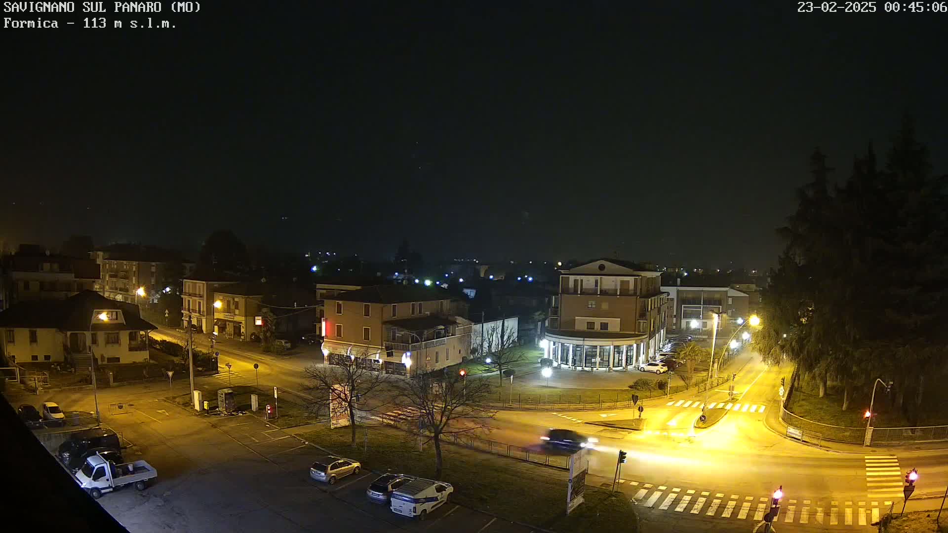 A nighttime, high-angle view of a town square with cars and buildings illuminated by streetlights under a dark, clear sky.