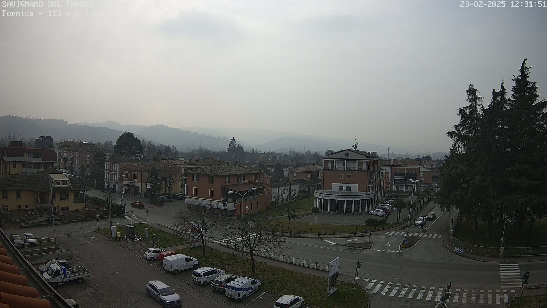 A hazy view of a town square and surrounding buildings, with hills in the background under an overcast sky.