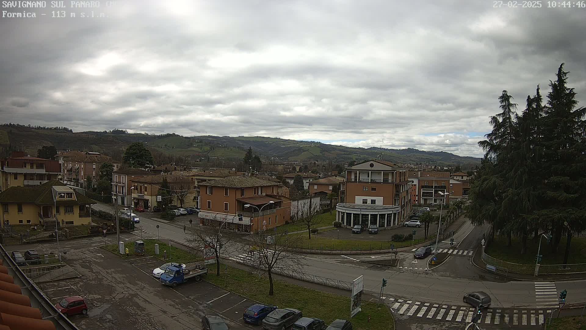 An overcast day reveals a town nestled in a valley, with low-lying buildings and rolling hills visible in the distance.