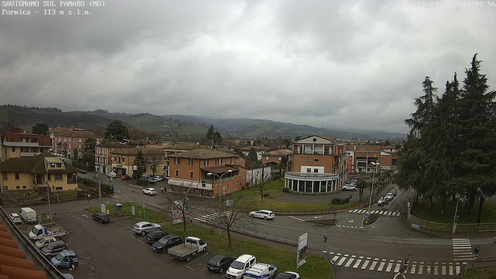 A mostly cloudy day reveals a town nestled in a valley, with cars parked in a lot and driving along roadways.
