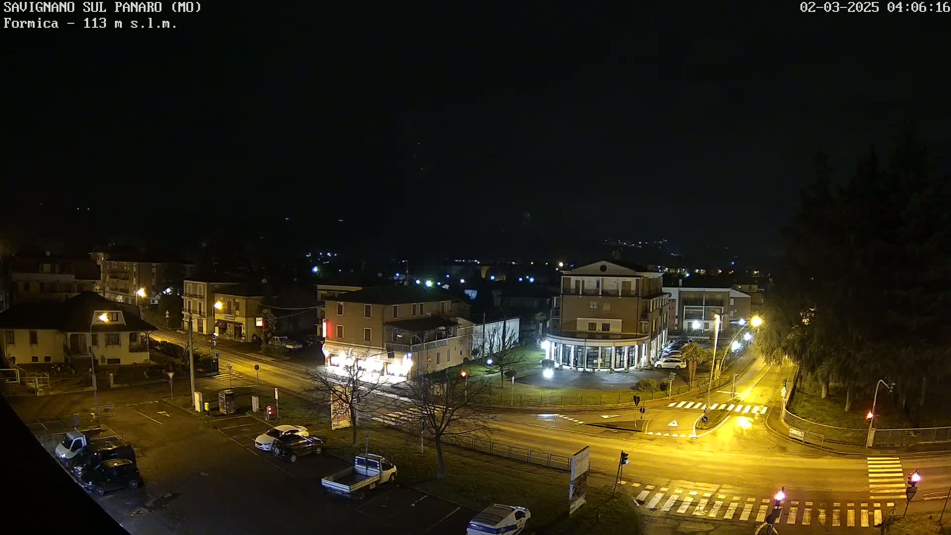 A nighttime, high-angle view of a town's street intersection and surrounding buildings, illuminated by streetlights.