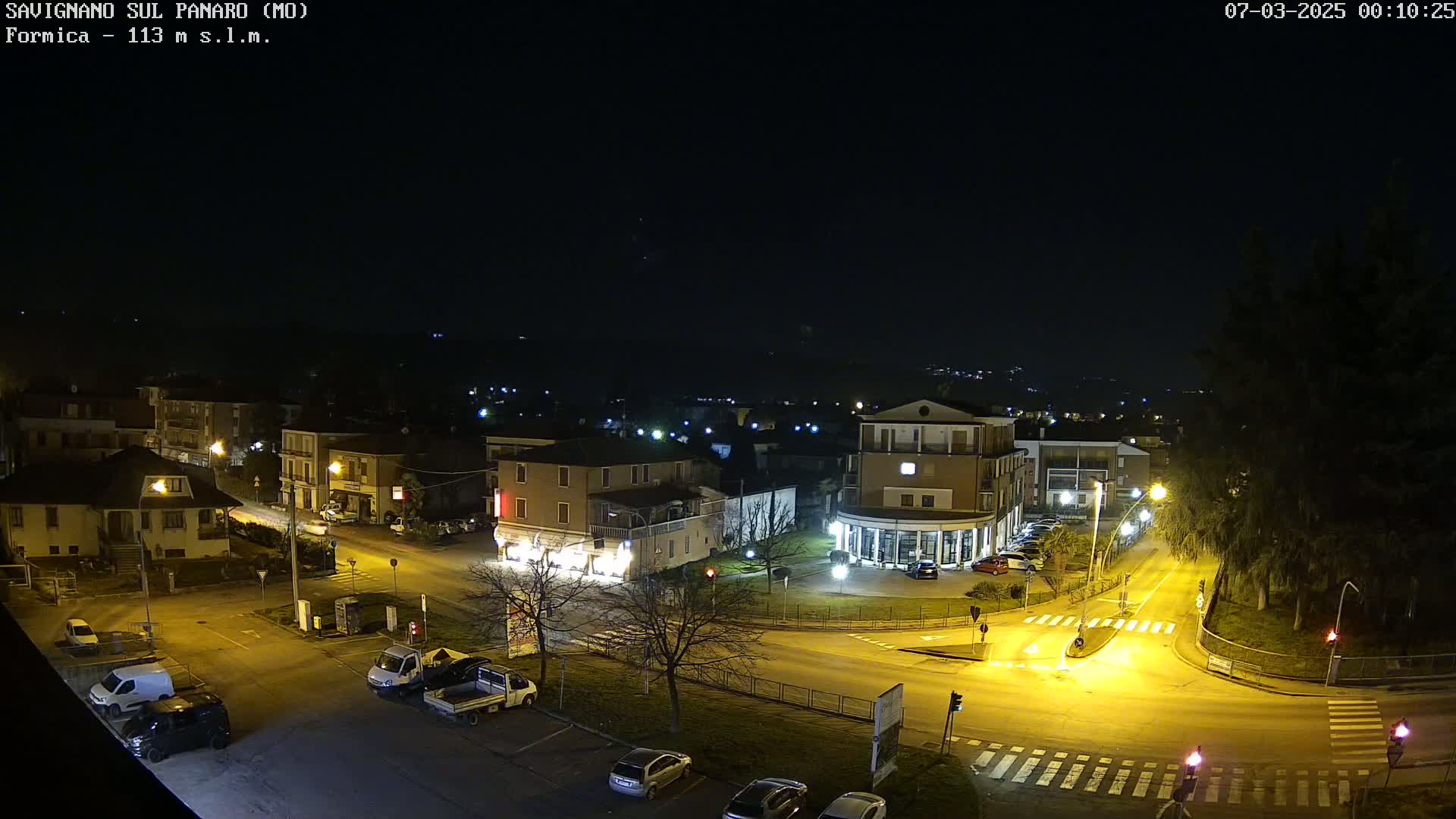 A nighttime, overhead view of a town square with several buildings, cars, and streetlights illuminated under a clear, dark sky.