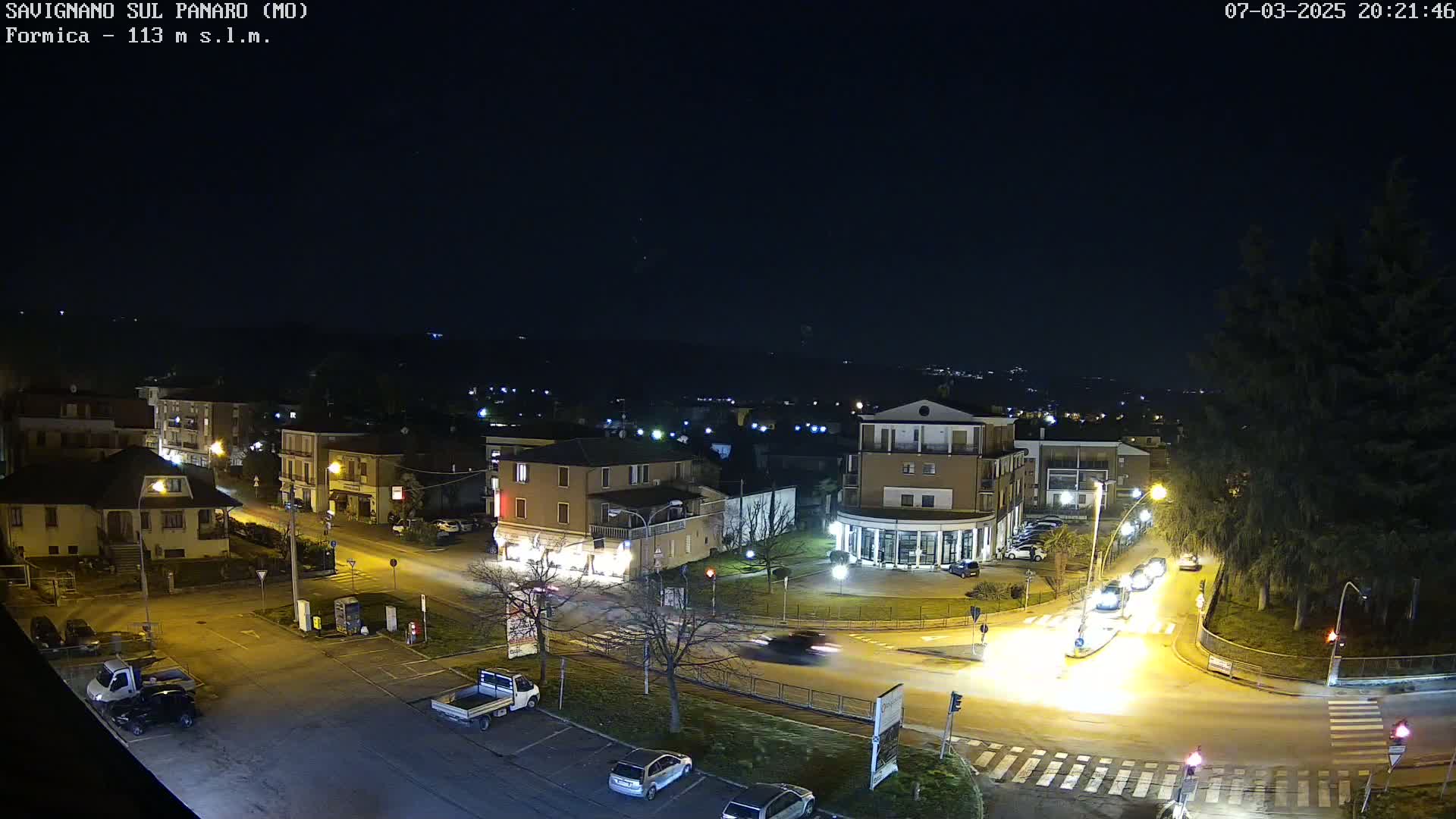 A nighttime, overhead view of a town's streets and buildings, with a few cars driving on the roads.
