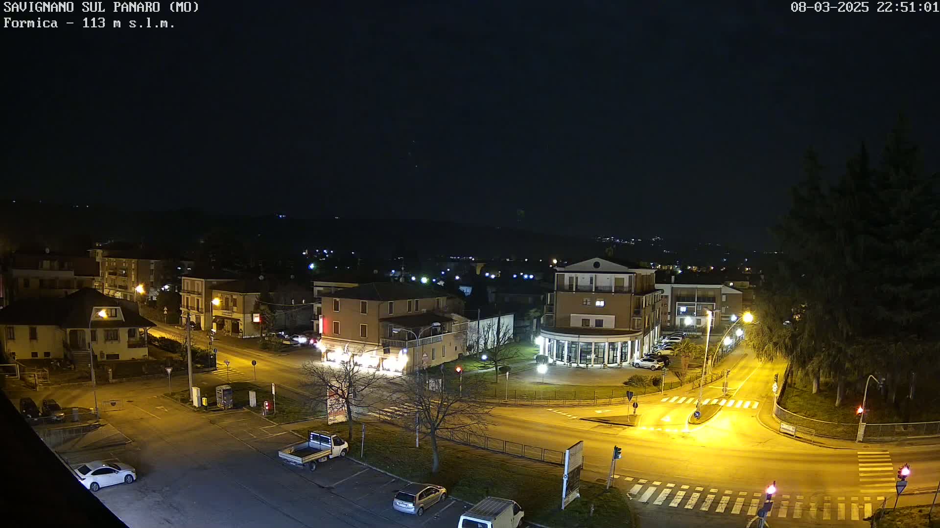 An aerial nighttime view of a town intersection with several cars and buildings illuminated under a clear, dark sky.