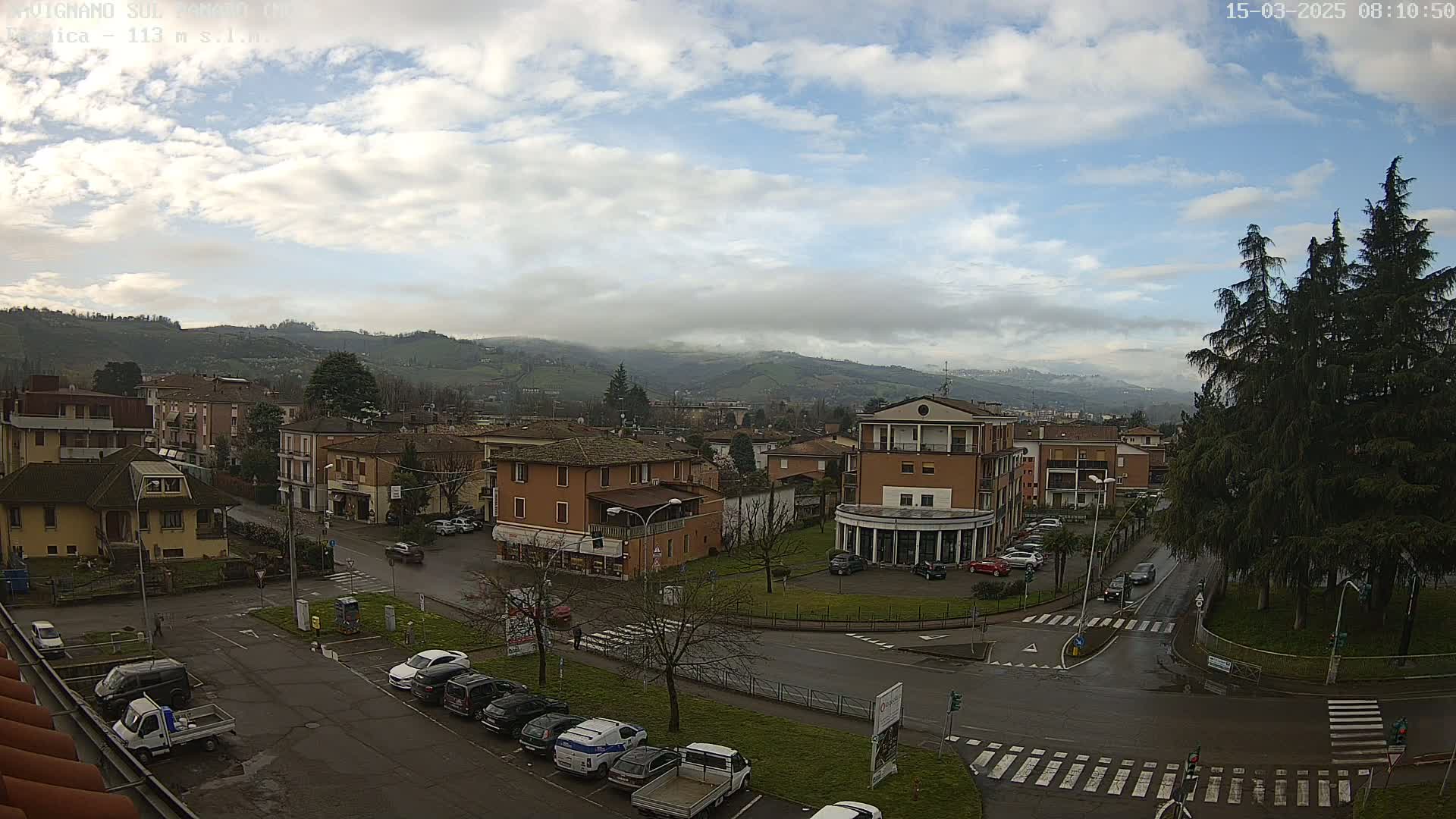 A partly cloudy day reveals a town nestled in a valley, with cars parked along streets and buildings of varying heights.