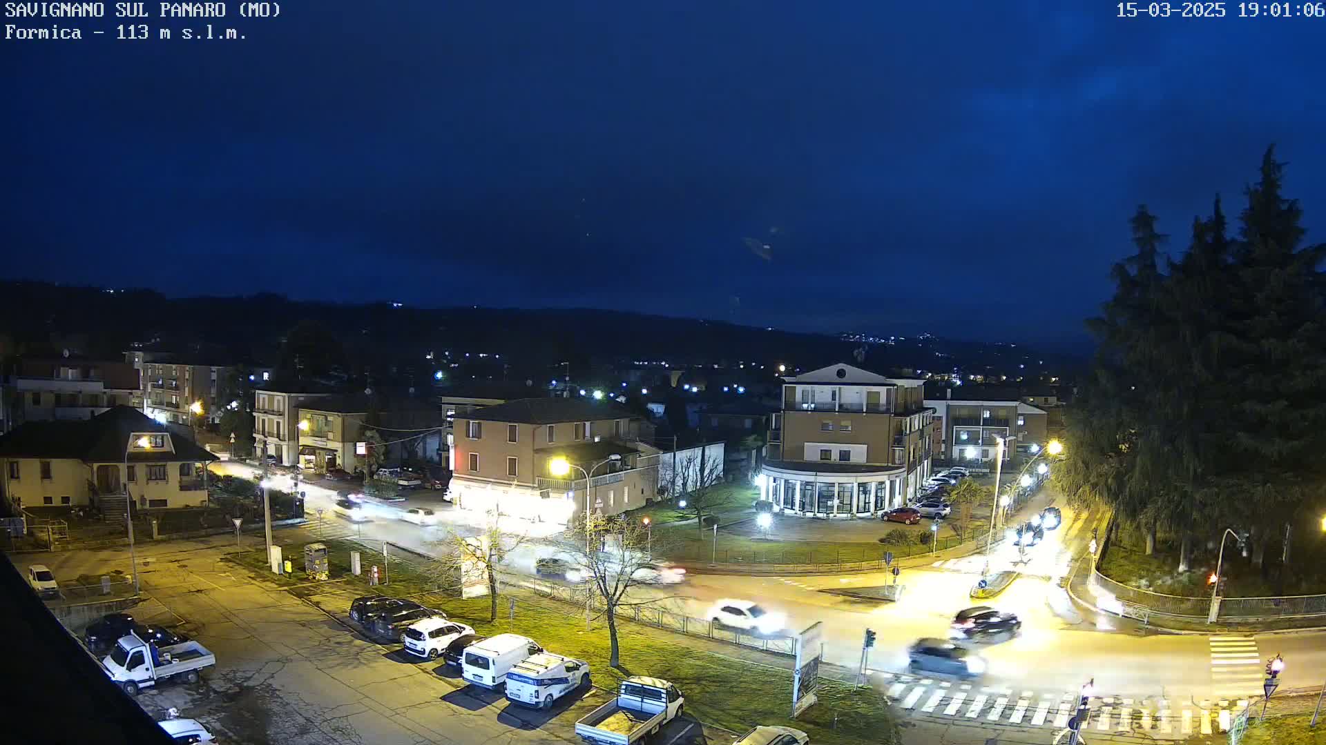 A nighttime aerial view of a town square with cars moving through an intersection under a clear, dark blue sky.