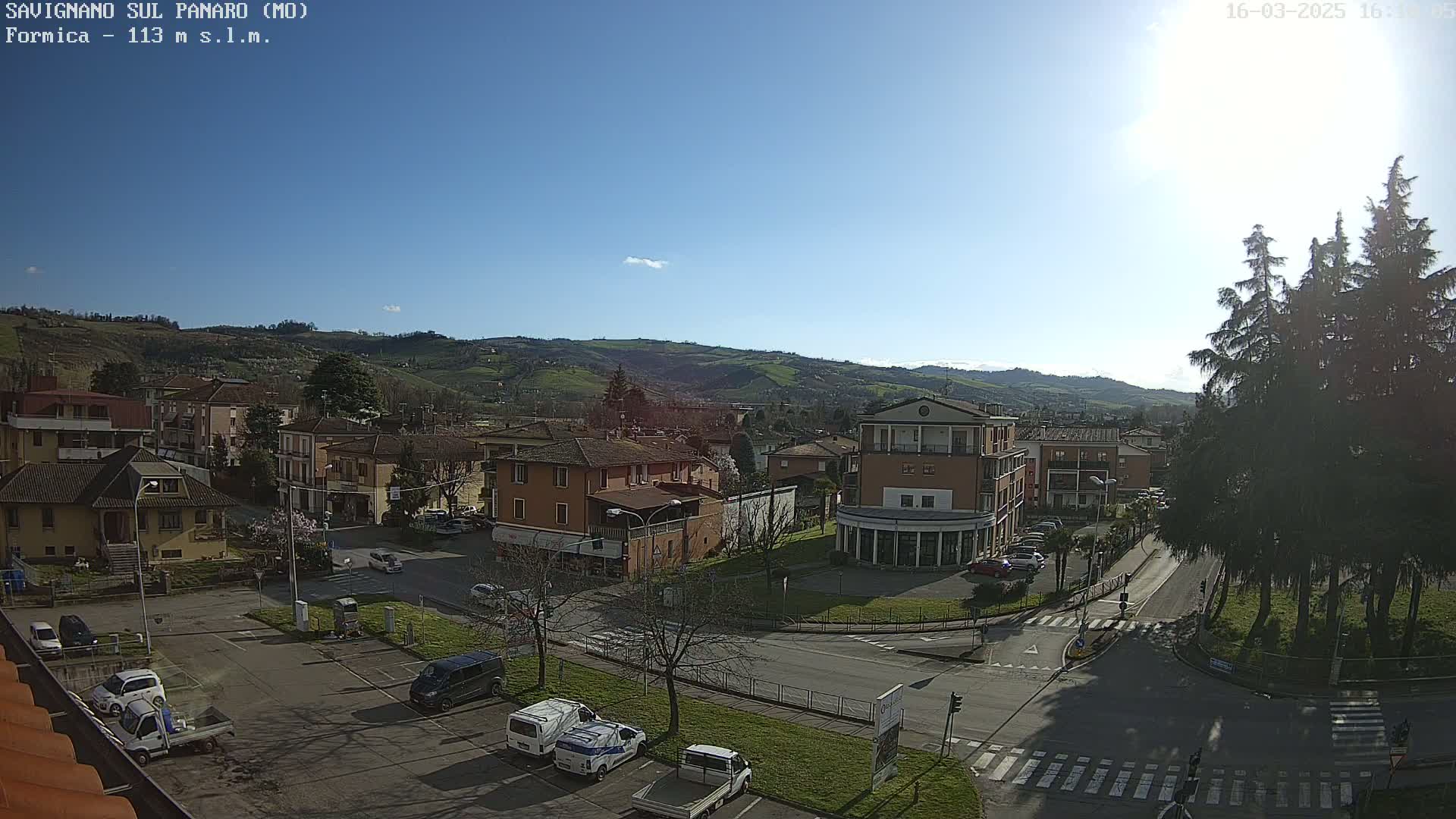 A sunny day overlooks a town nestled in a valley, with cars parked in a lot and buildings surrounding a paved intersection.