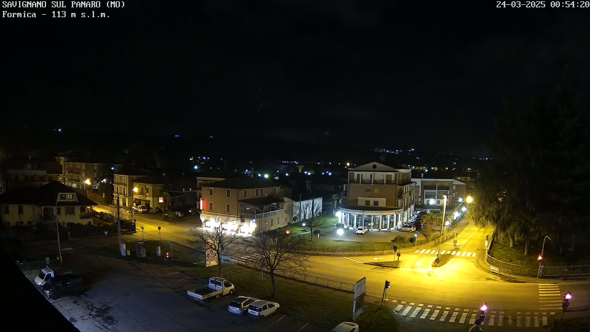 A nighttime, overhead view of a town square with several buildings and cars, illuminated by streetlights under a clear, dark sky.