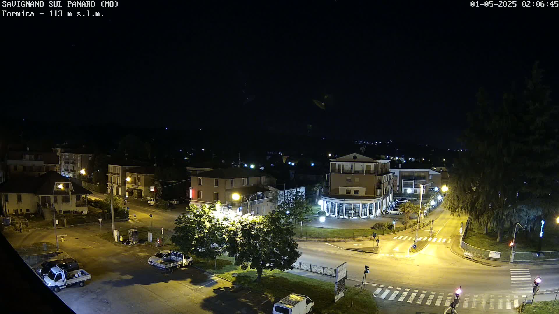 A nighttime, high-angle view of a town intersection with buildings and vehicles, illuminated by streetlights.