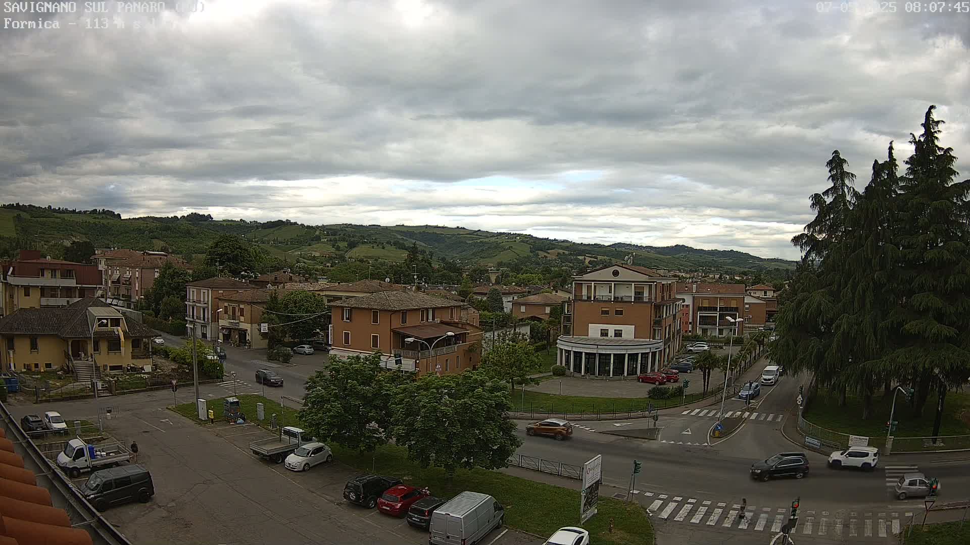 An overcast day reveals a town nestled in a valley, with cars navigating streets and parking lots surrounded by buildings and greenery.