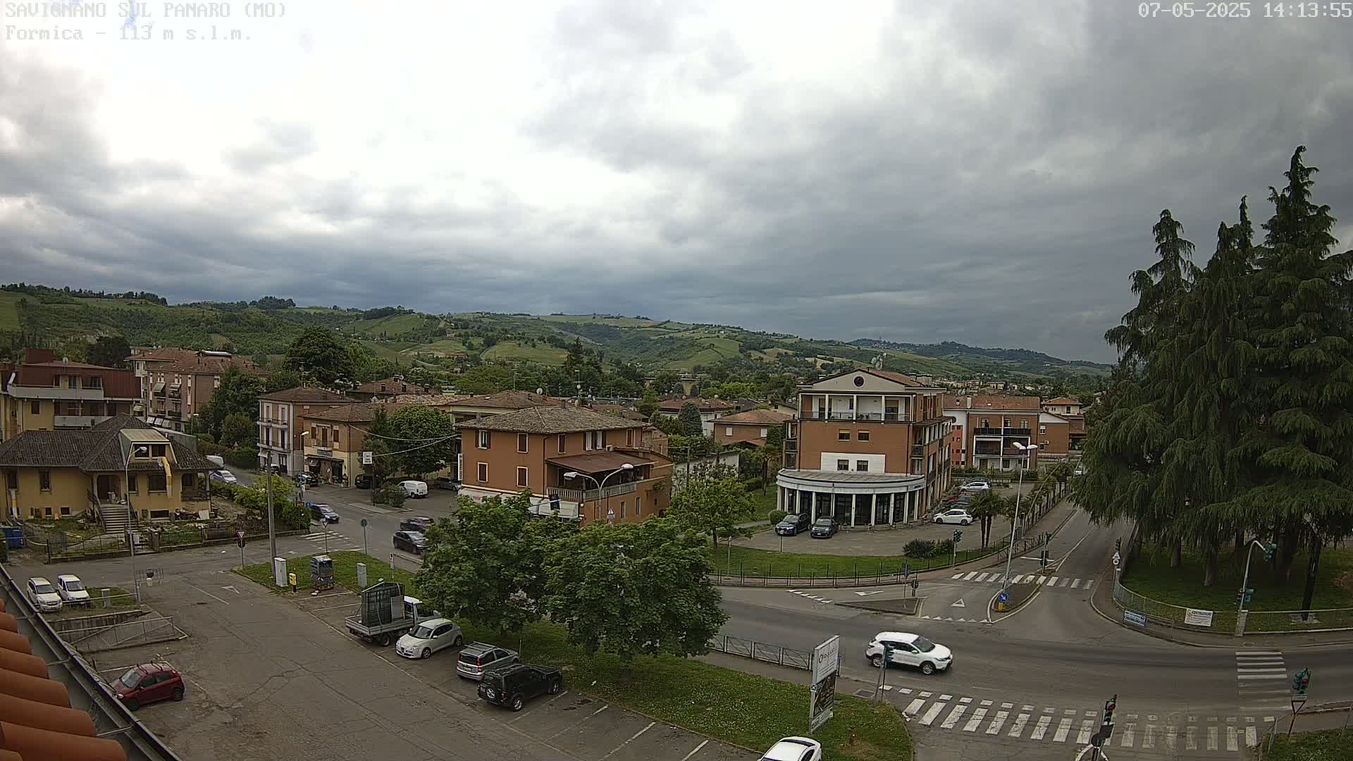 A mostly cloudy day reveals a small town nestled in a valley, with cars parked in lots and driving on streets that curve through the area.