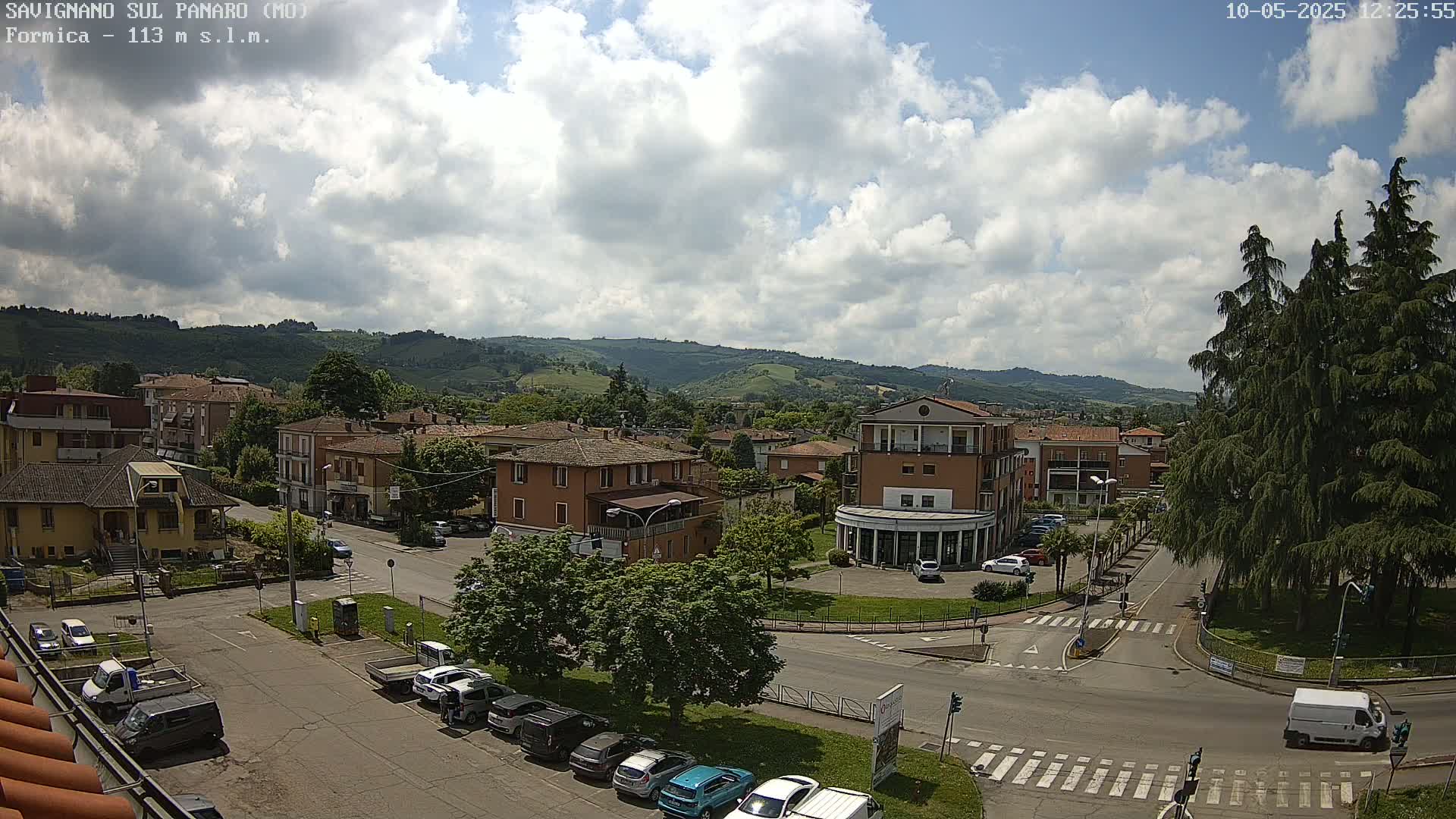 A partly cloudy day reveals a view of a town nestled in a valley, with cars parked along streets and buildings of varying heights.