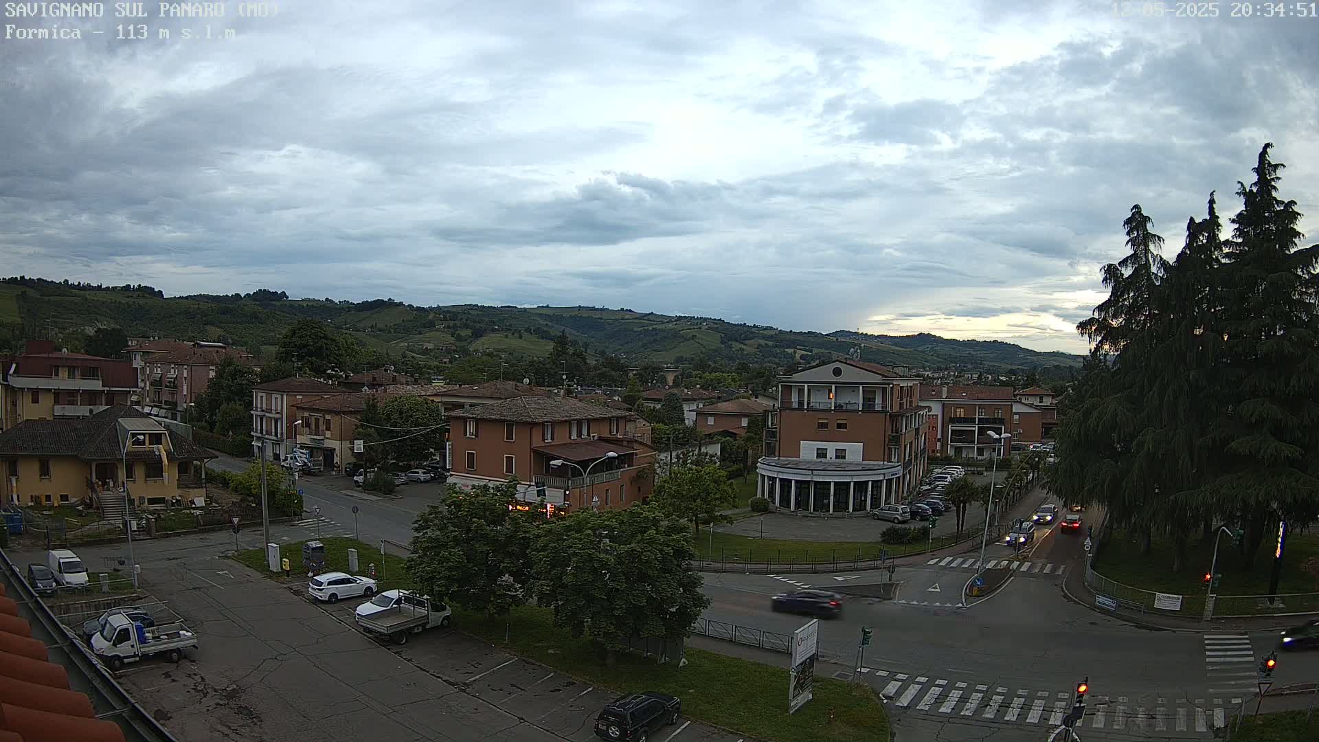 An overcast sky hangs over a town nestled in a valley, with cars moving along its streets.