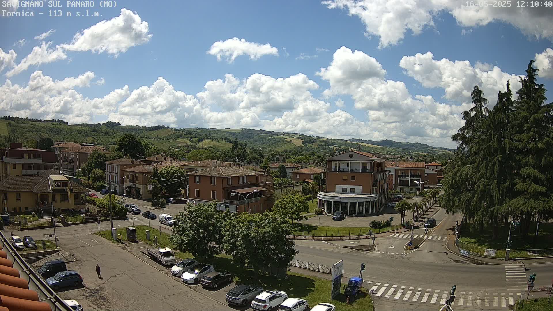 A partly sunny day reveals a small town nestled in a valley, with numerous buildings and cars visible from a high vantage point.