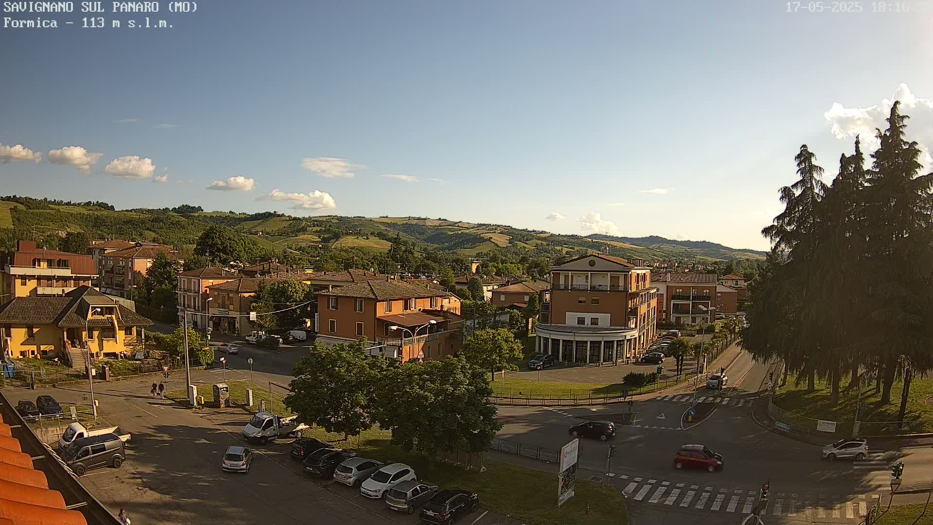 A sunny day reveals a town nestled in a valley, surrounded by rolling green hills and a few cars traveling on the roads.