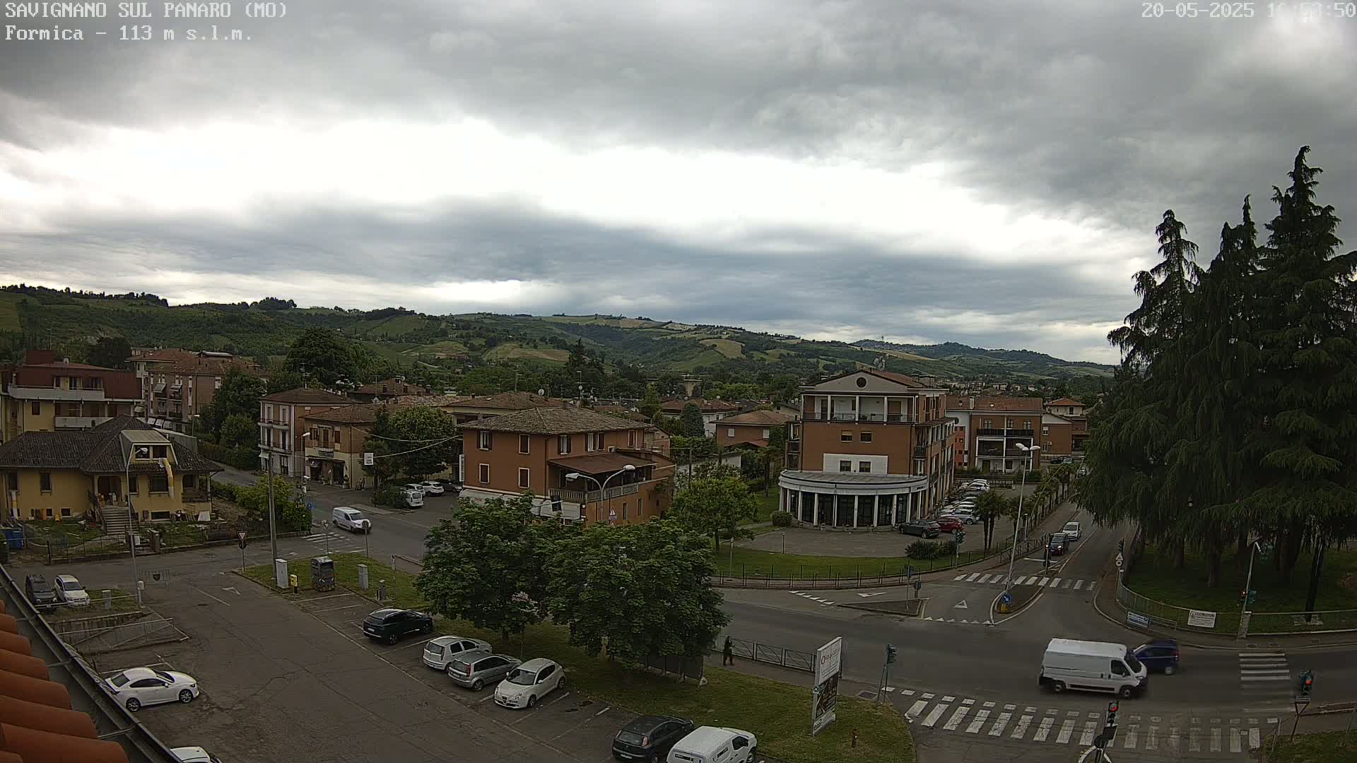 An overcast sky hangs over a town nestled in a valley, with cars parked in lots and driving on streets.