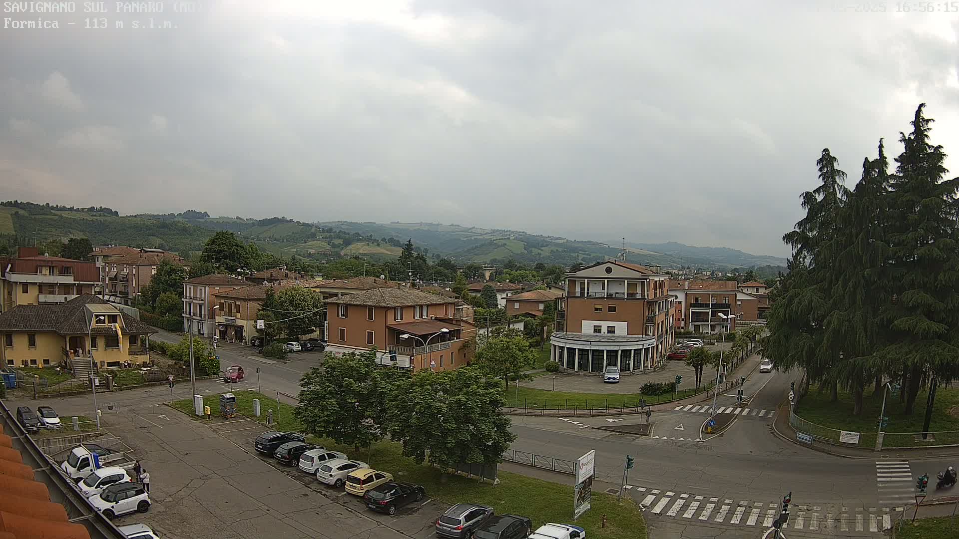An overcast day reveals a town nestled in a valley, with cars parked along streets and buildings surrounded by lush greenery.