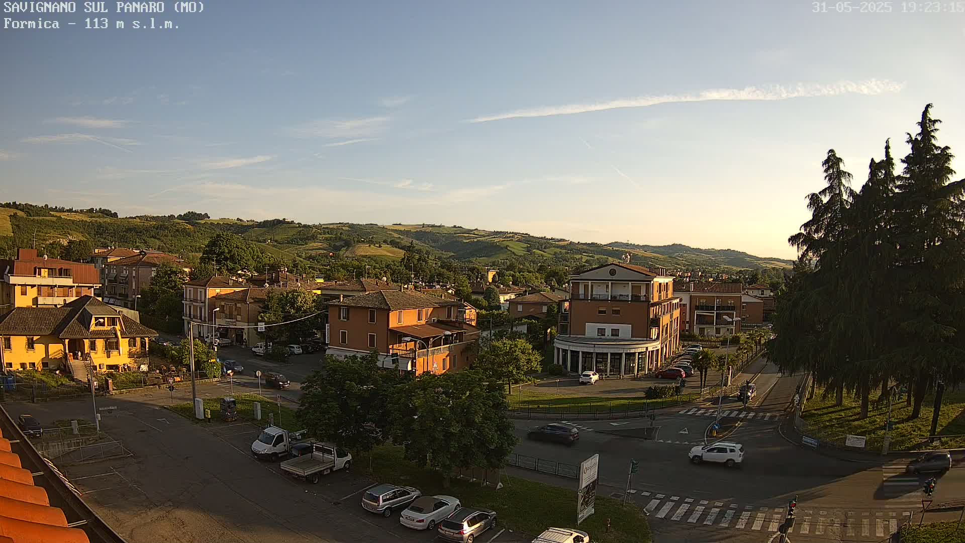 An elevated view of a town nestled in a valley under a clear, bright sky, with cars parked and driving on roads near several buildings.