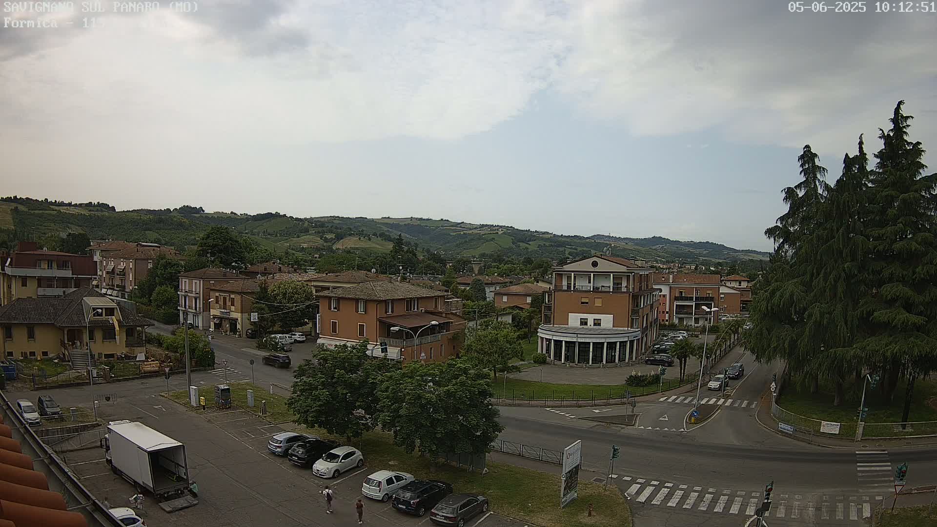 An overcast day reveals a small town nestled in a valley, with cars parked in lots and a few pedestrians strolling near buildings.
