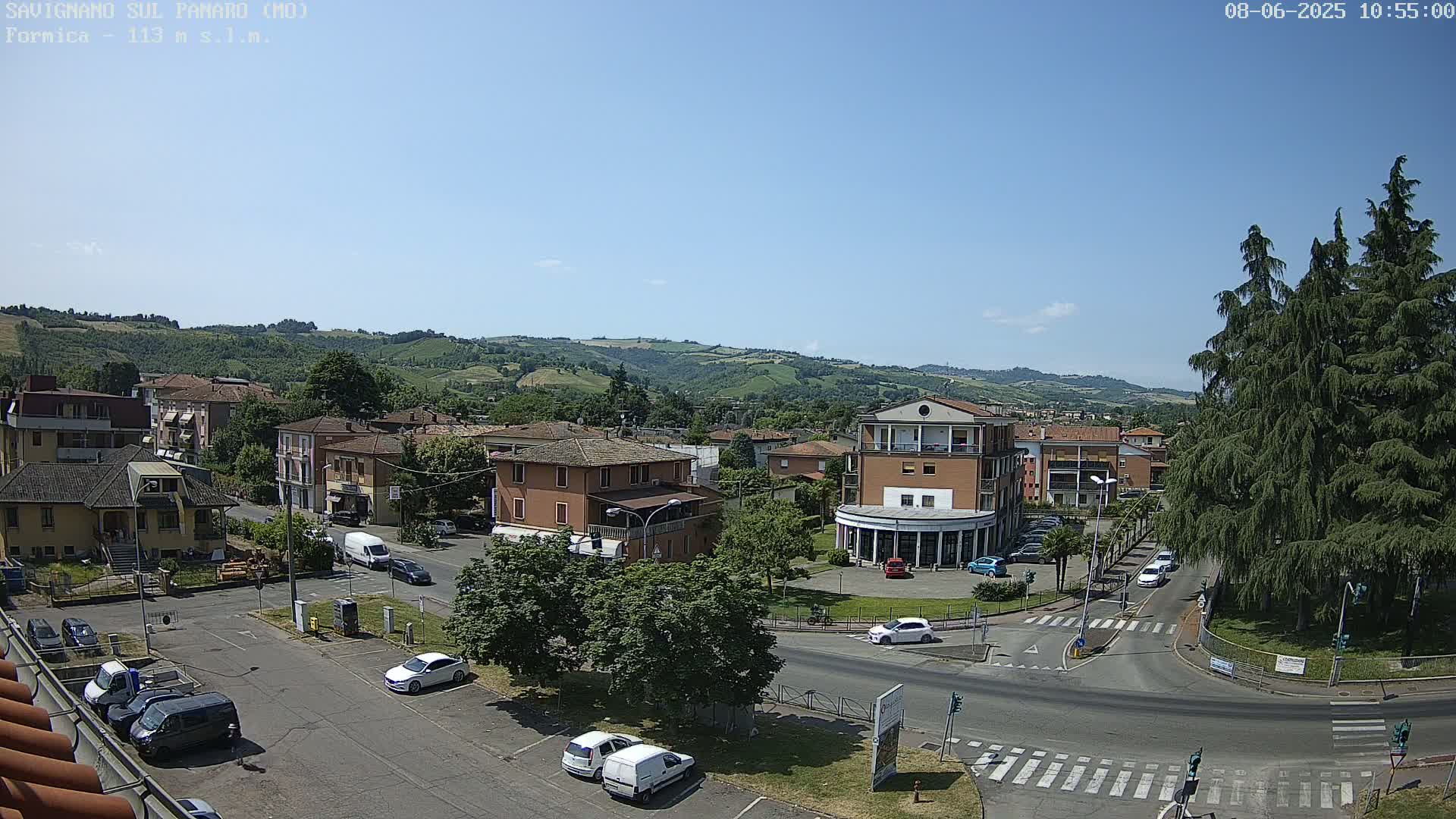 A sunny day reveals a town nestled in a valley, with buildings, cars, and trees visible from an elevated vantage point.