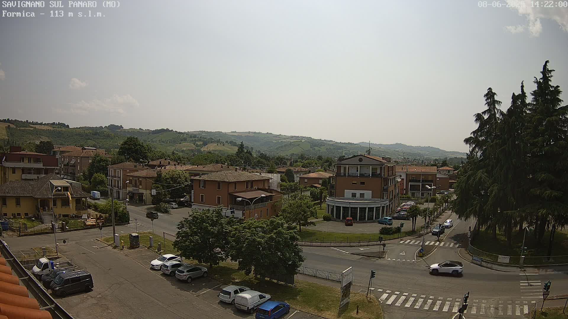 A mostly sunny view of a town nestled in a valley, with cars parked in lots and driving on the streets below.