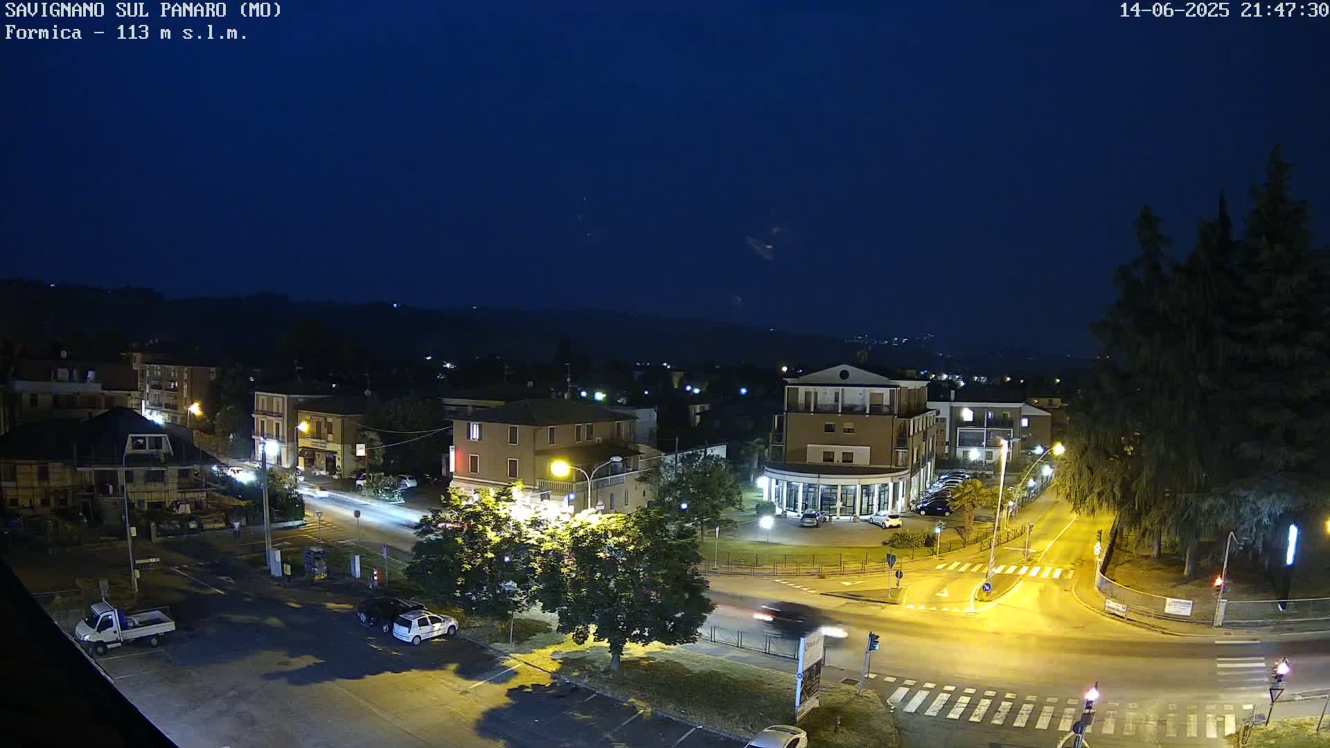 A sunny, hazy day reveals a town nestled in a valley, with rolling hills in the background and cars parked in a paved lot in the foreground.