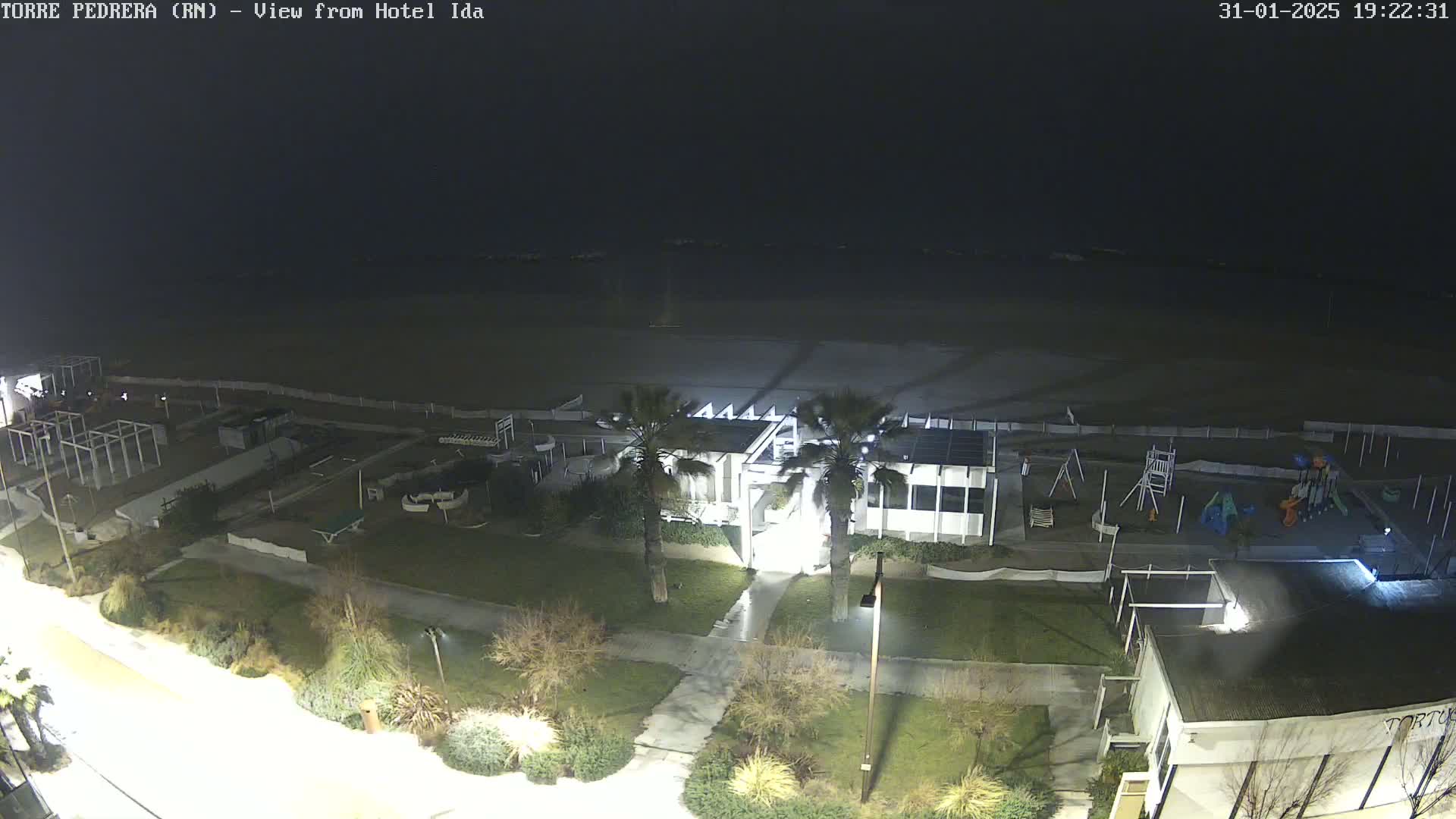 A nighttime aerial view shows a beach, playground, and building complex next to a dark ocean under a clear sky.