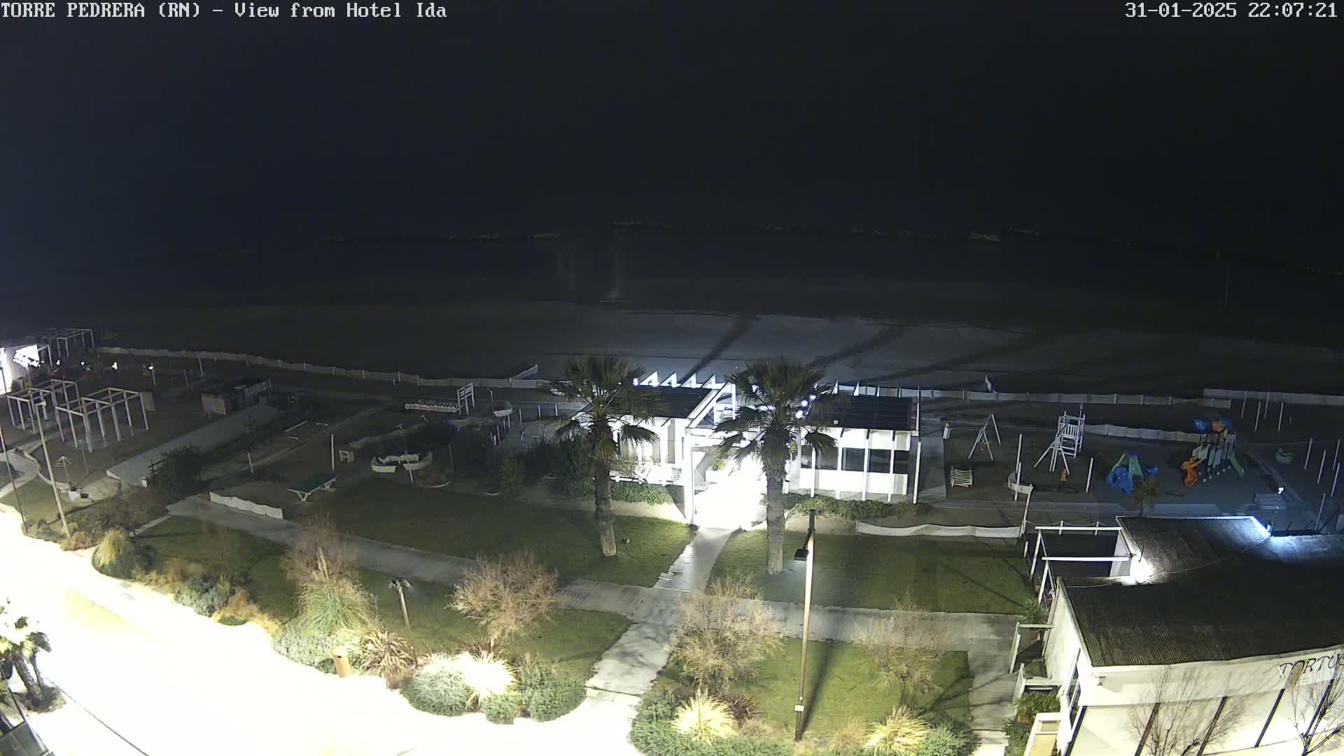 A nighttime, overhead view of a beach, playground, and buildings, illuminated by artificial light.