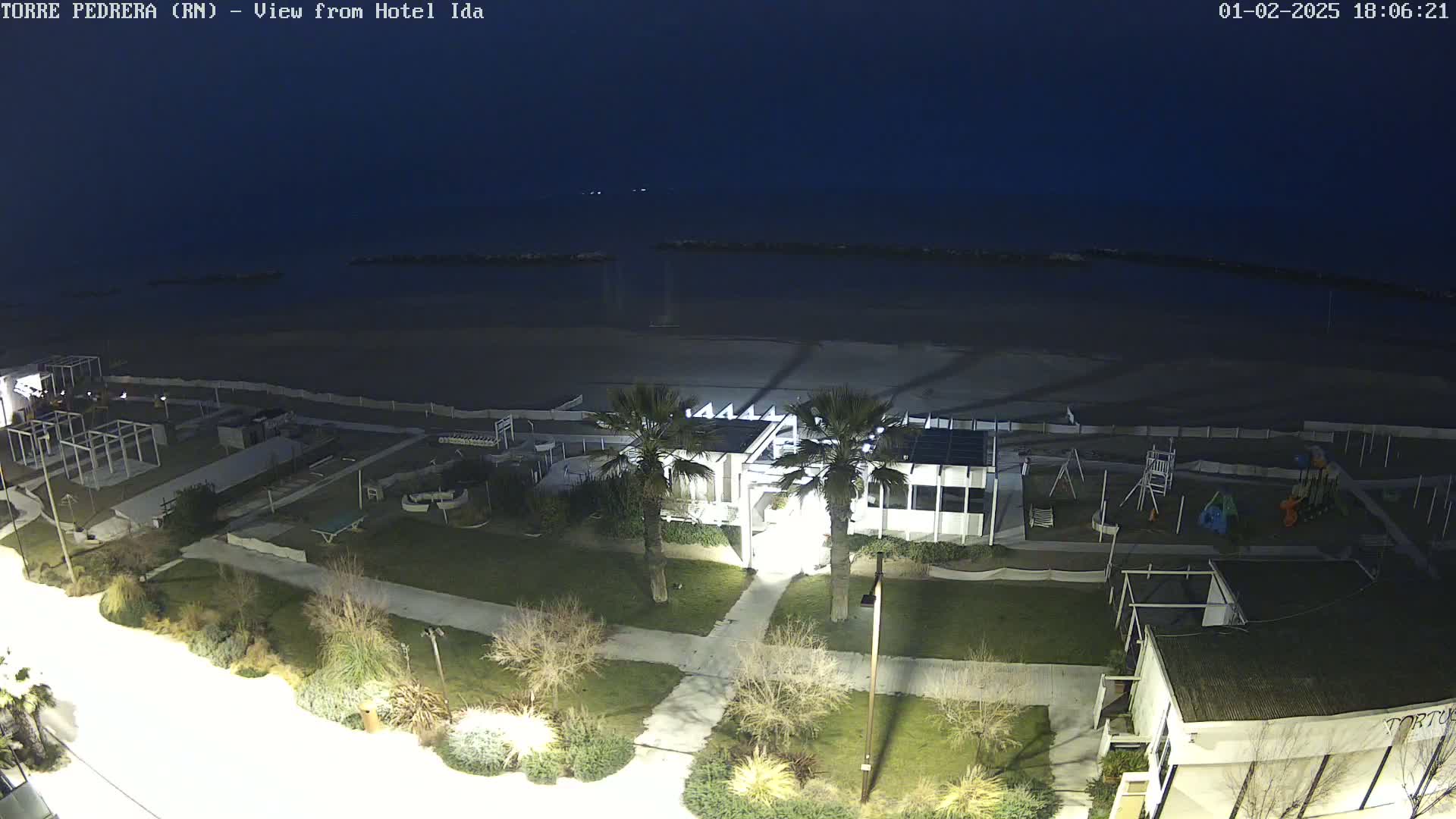 A nighttime view of a beach with a building, playground, and palm trees, under a dark, clear sky.