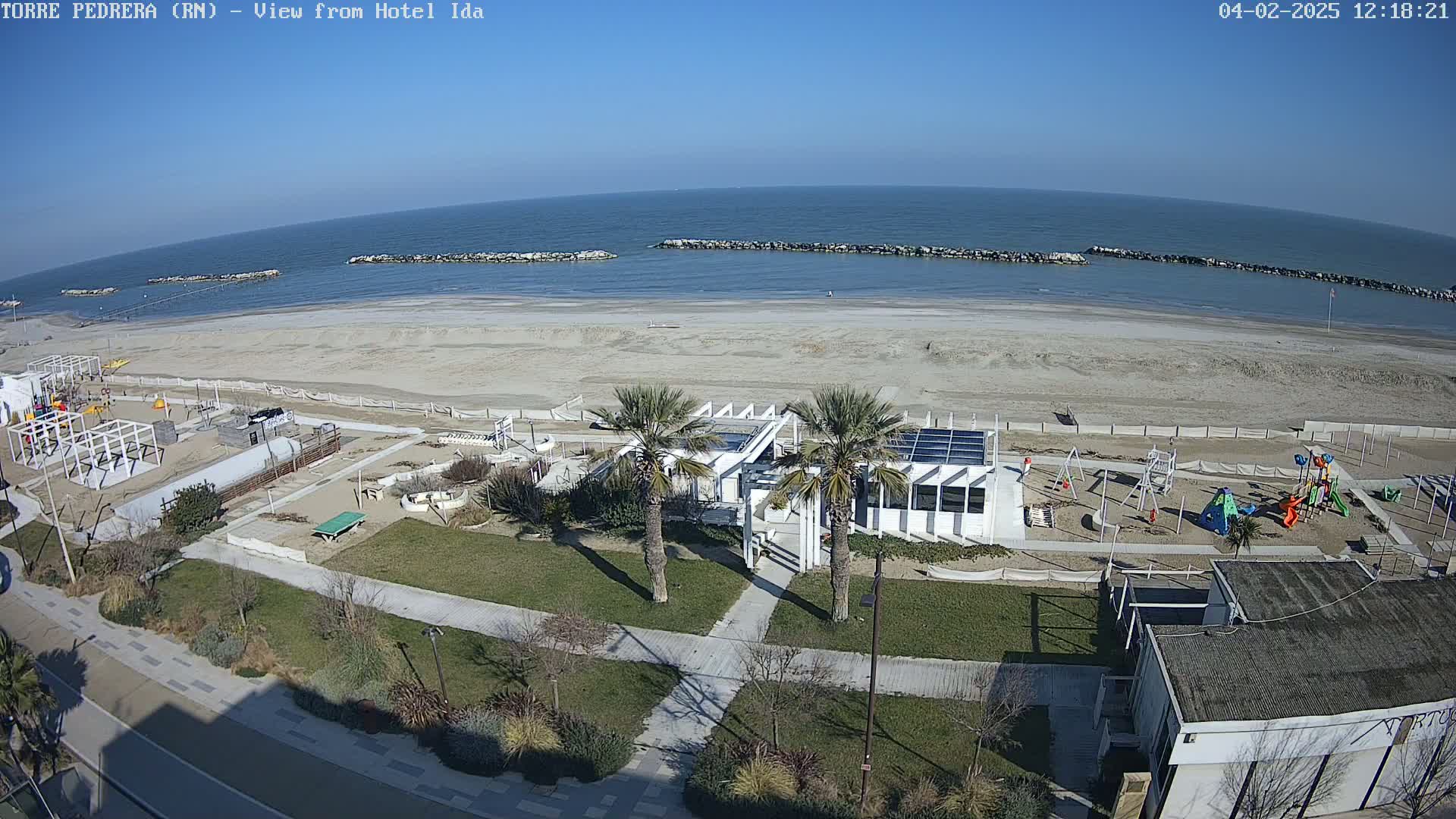 A beach with a playground and a building is seen from above on a sunny day.